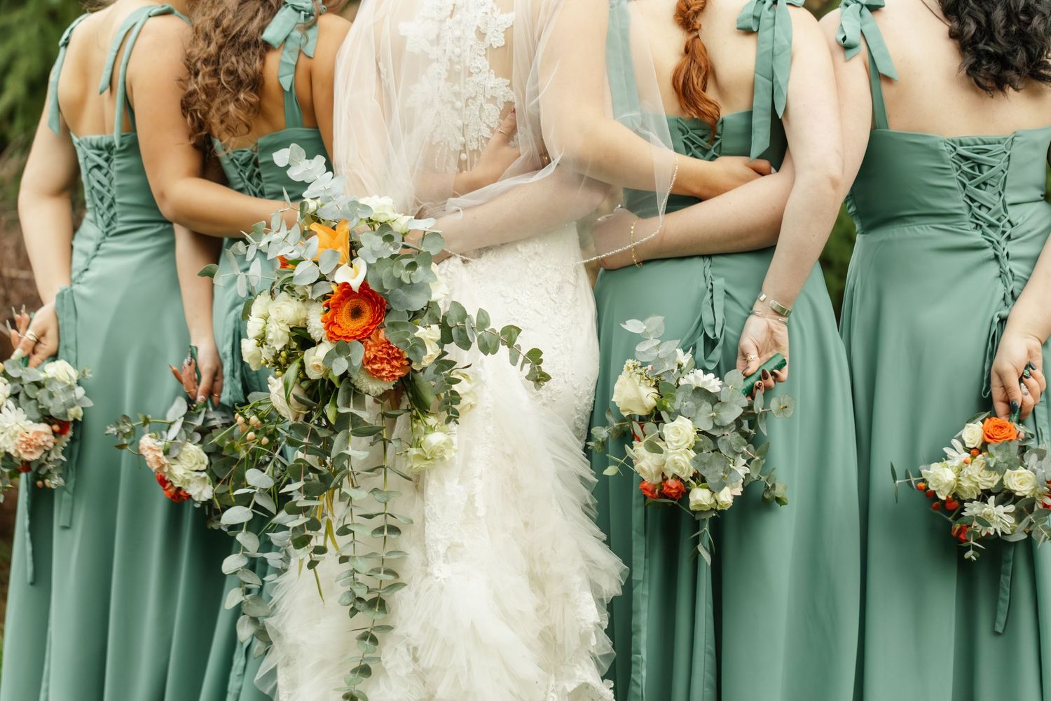 Wedding party wearing sage green bridesmaid dresses holding colorful bouquets with orange and white flowers.