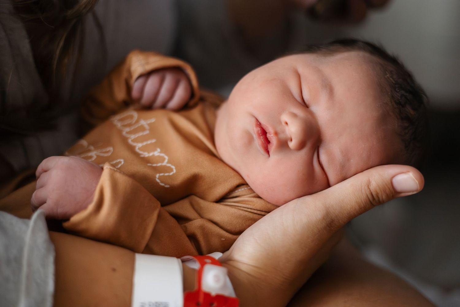 Peaceful newborn baby sleeping in brown outfit with soft lighting.