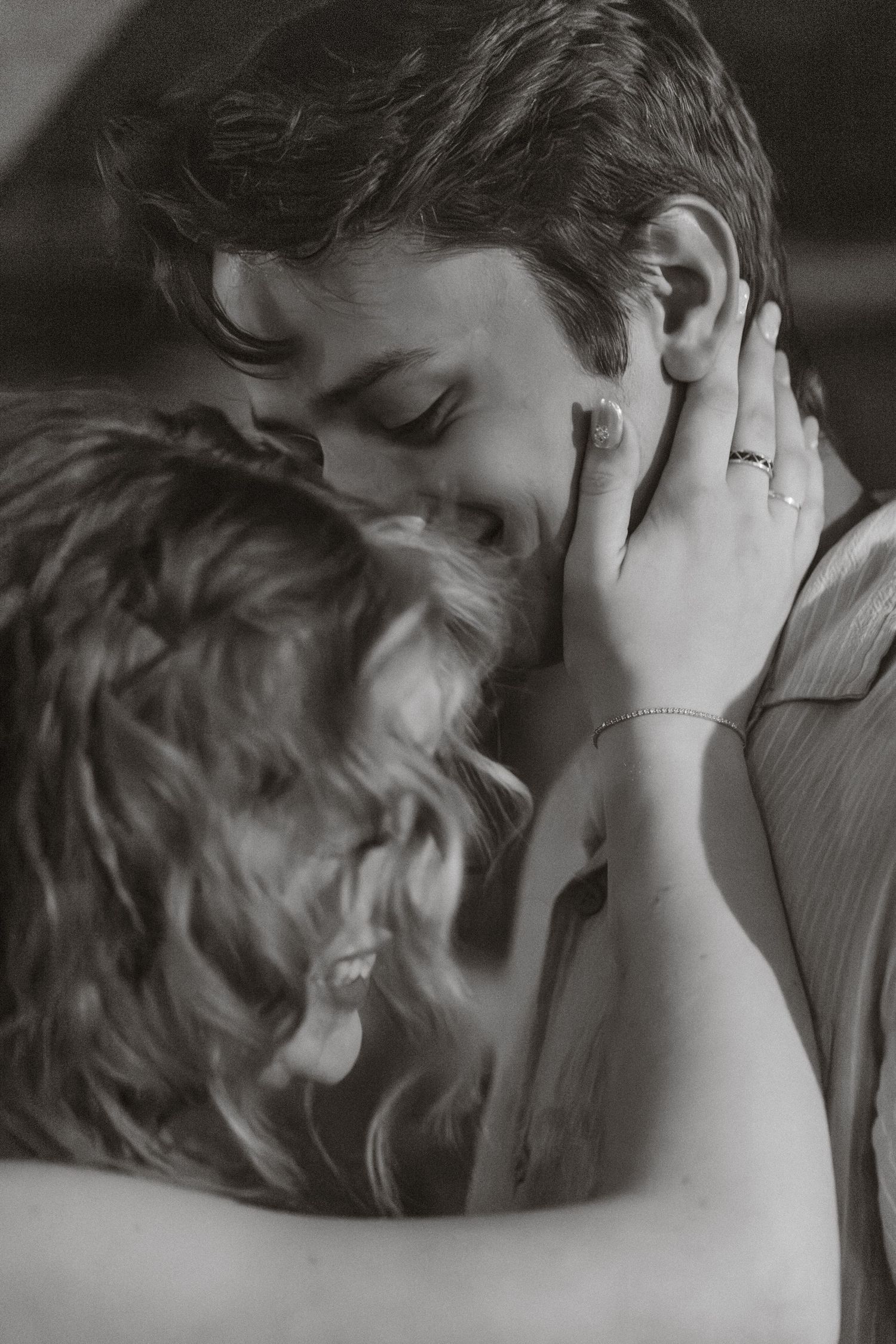 Black and white photo of a couple embracing intimately, woman tenderly holding man's face with ring on finger.