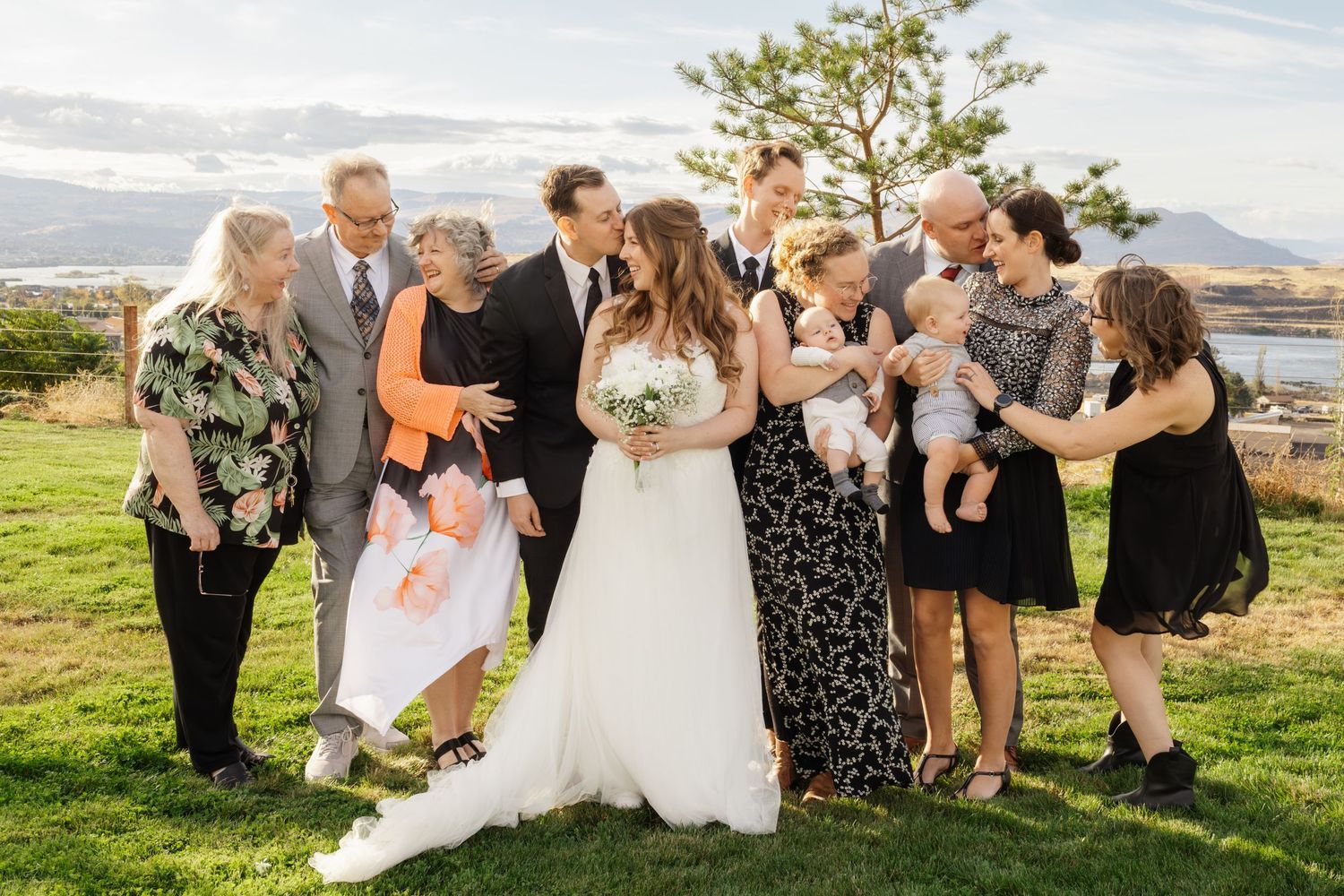 Wedding party gathered on grassy lawn by the ocean sharing laughter and joy with the newlyweds.