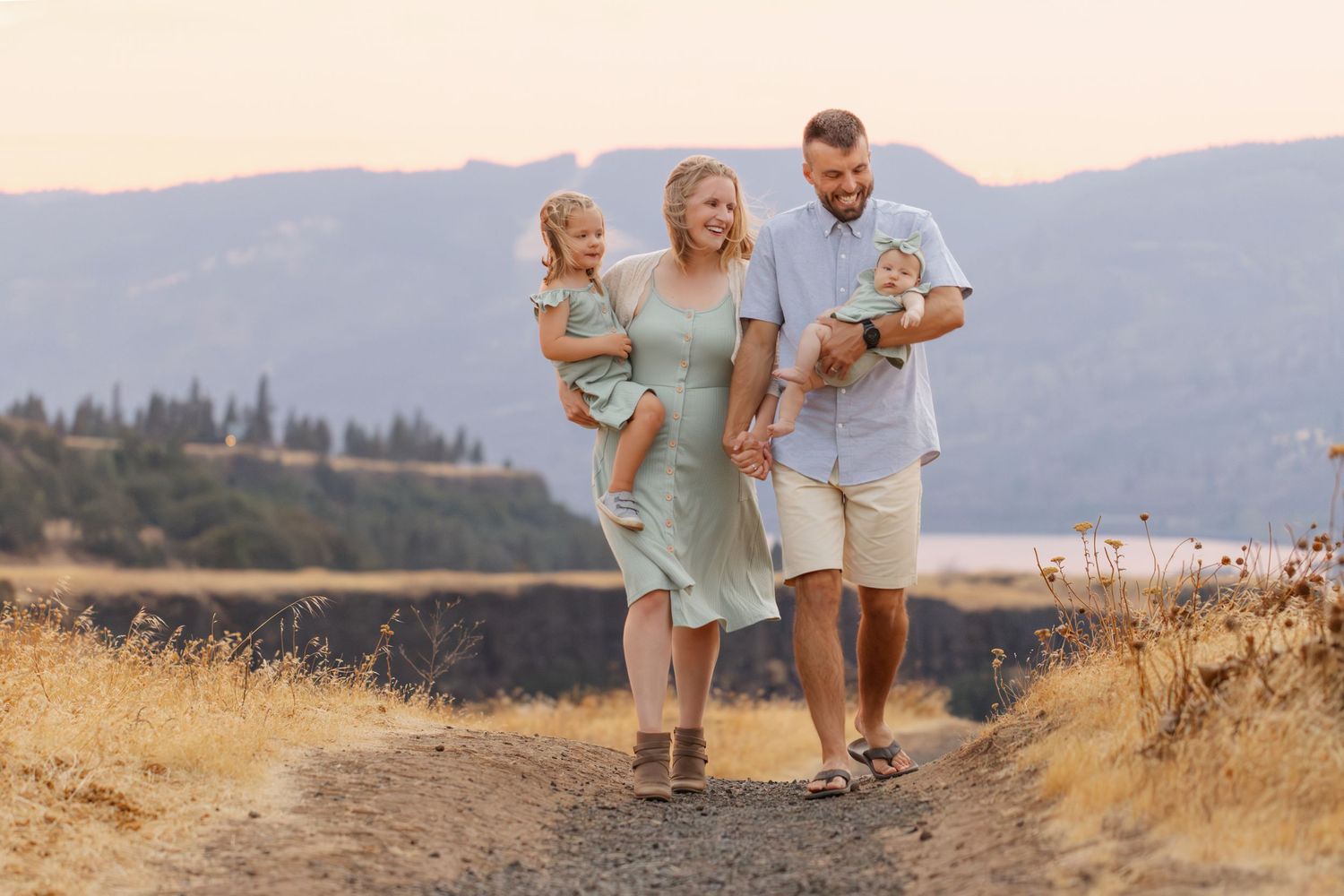 Family walking together on dirt path with mountain landscape behind them.