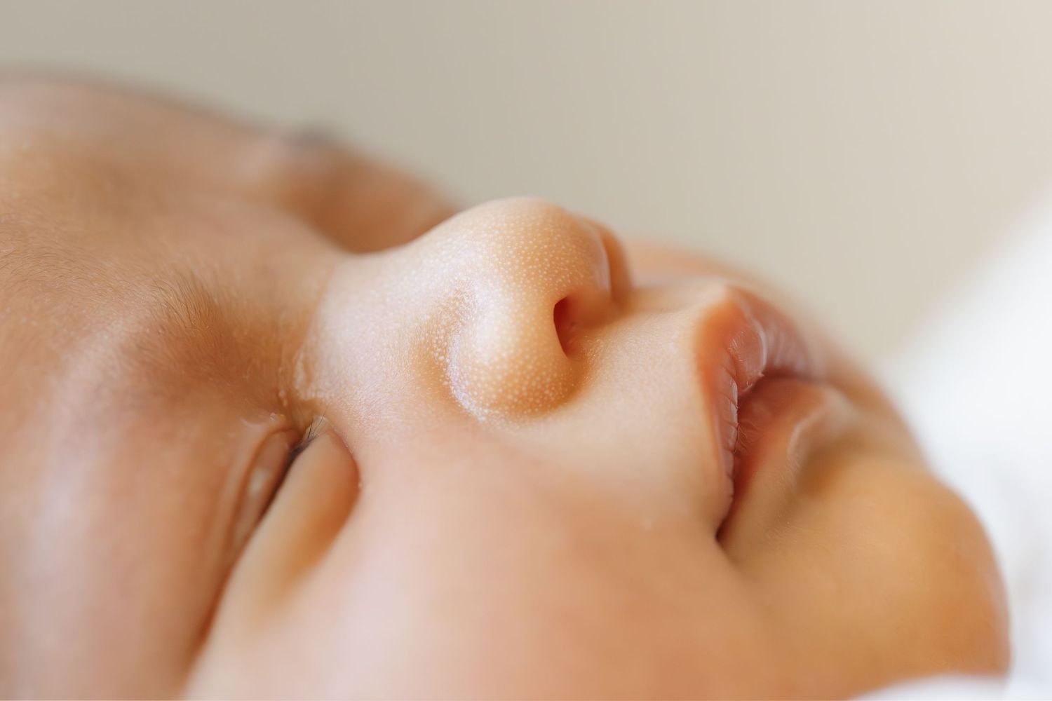 Close-up profile view of a sleeping infant's face against soft white background.