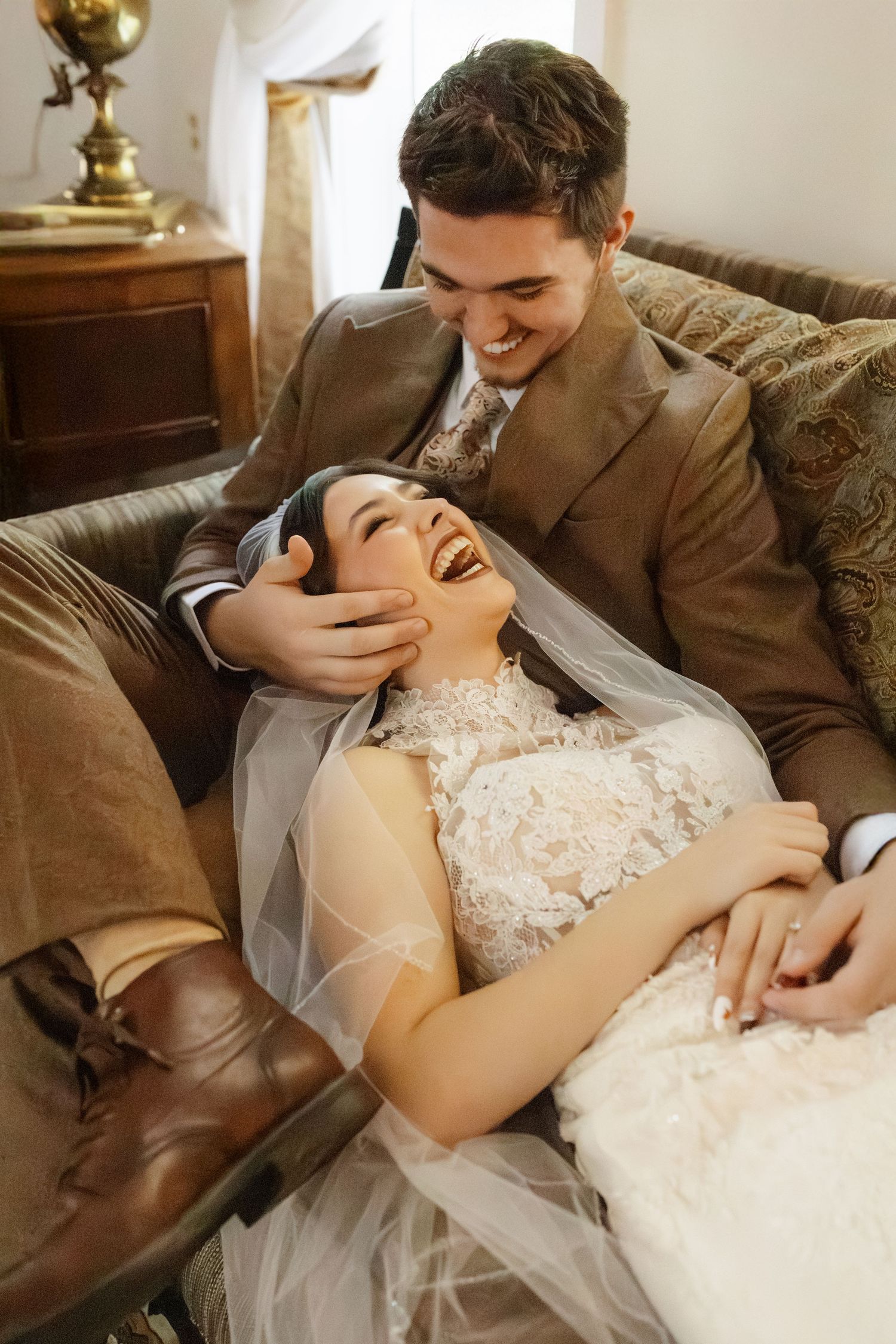 Intimate wedding couple shares tender moments while reclining on a vintage couch in their formal attire.