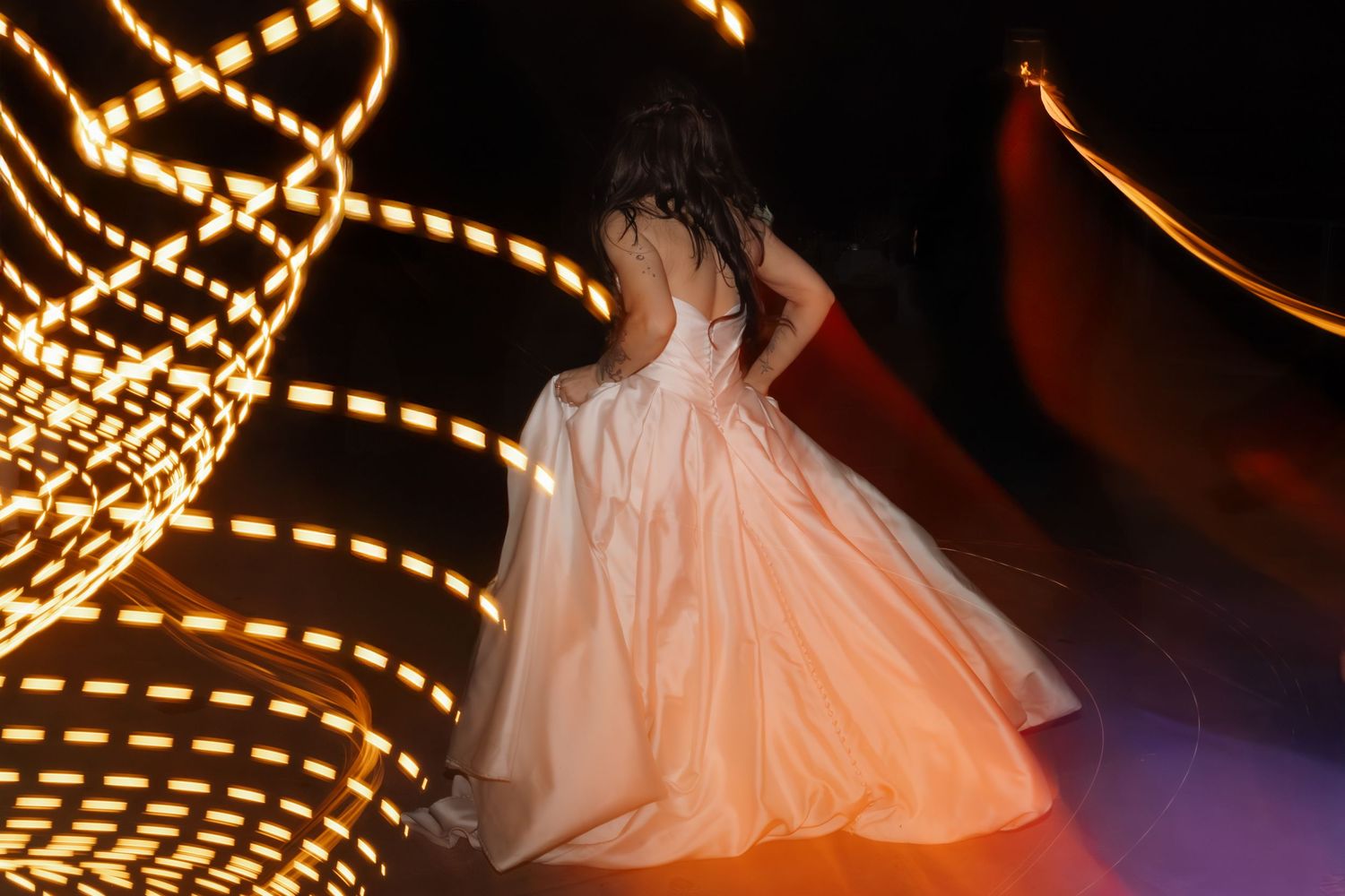 Illuminated string lights create a bokeh effect against a dark background with blurred silhouettes dancing below.