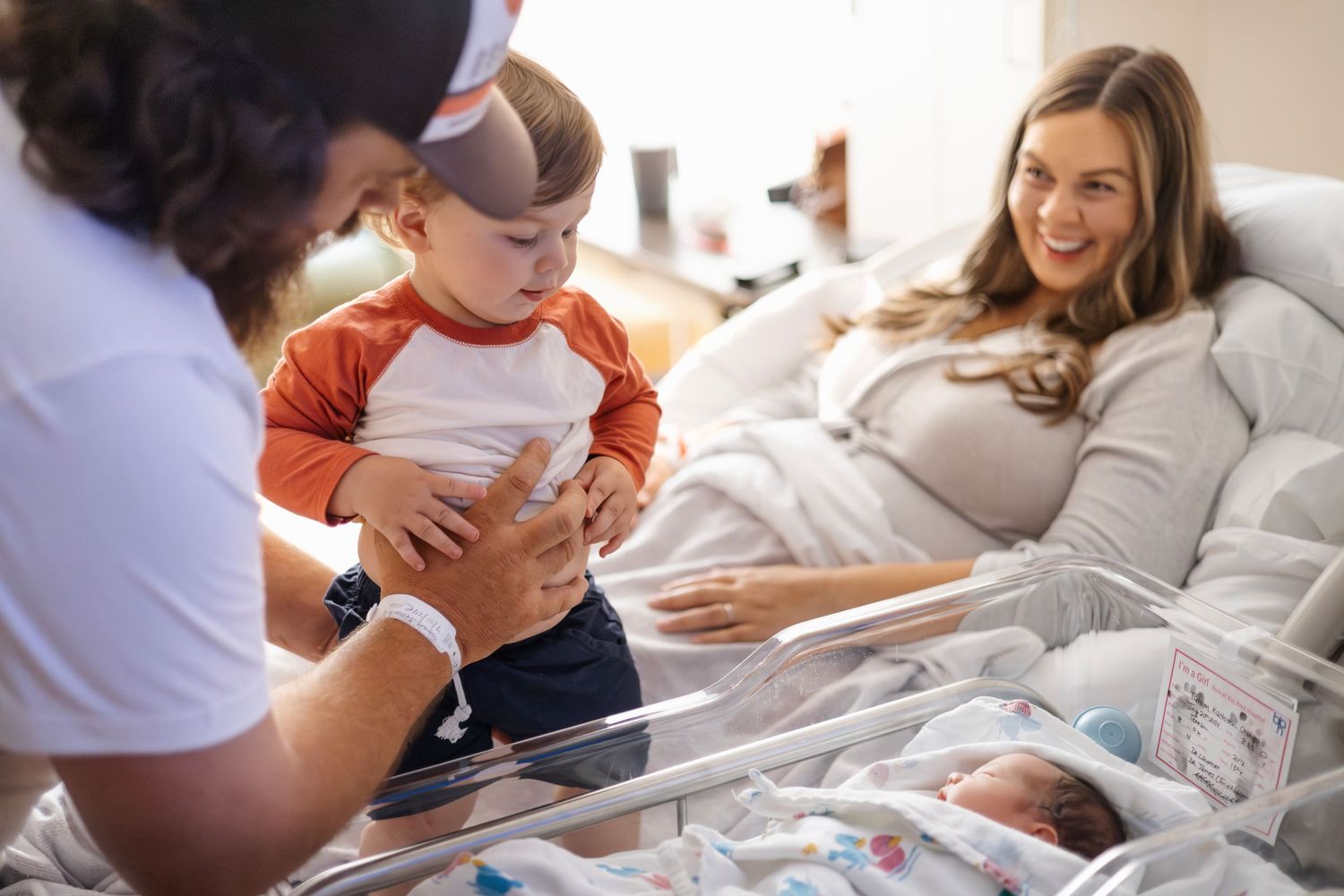 Healthcare worker examines newborn baby in hospital bassinet while others look on with joy.
