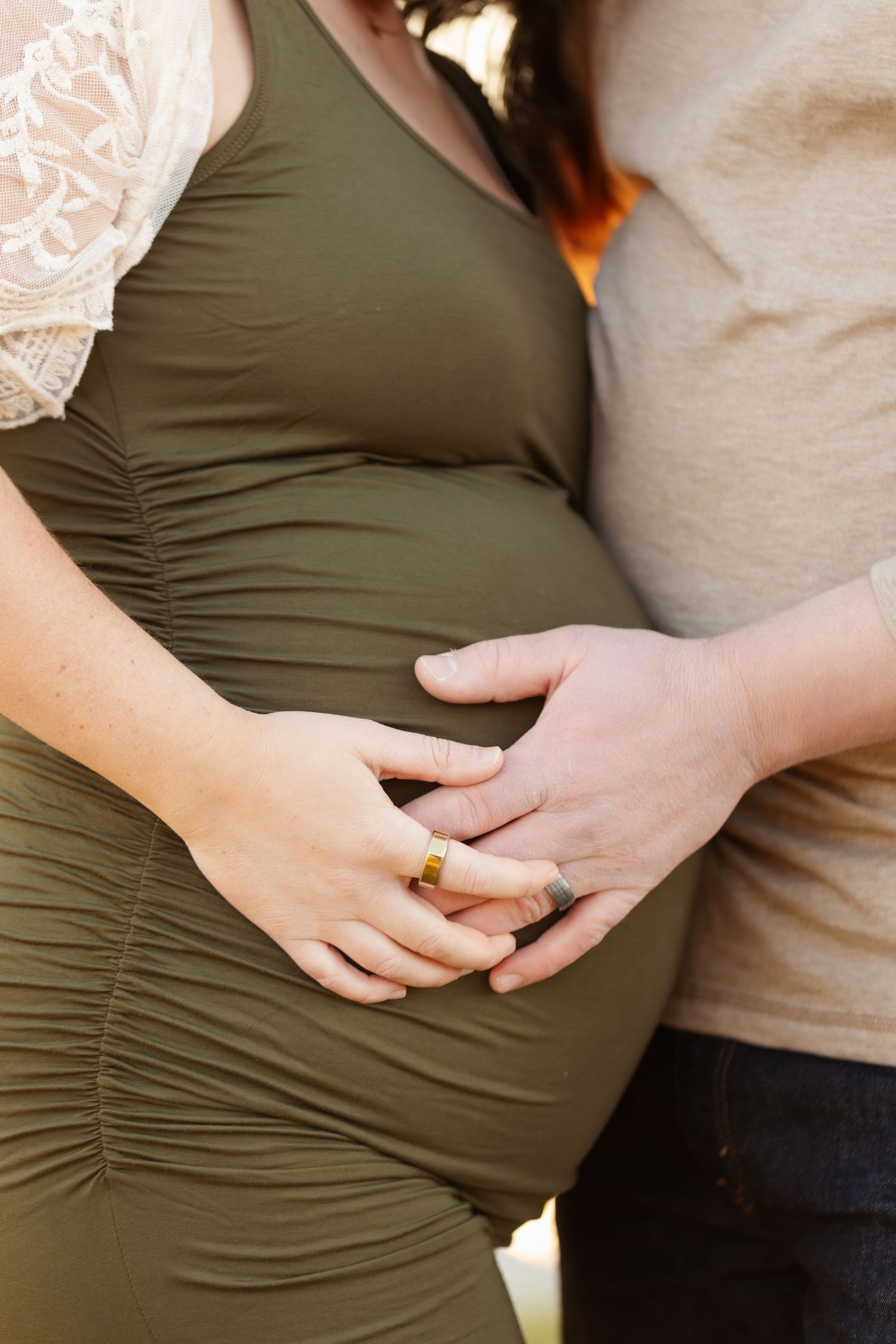 Close-up of hands cradling pregnant belly while wearing olive green dress.