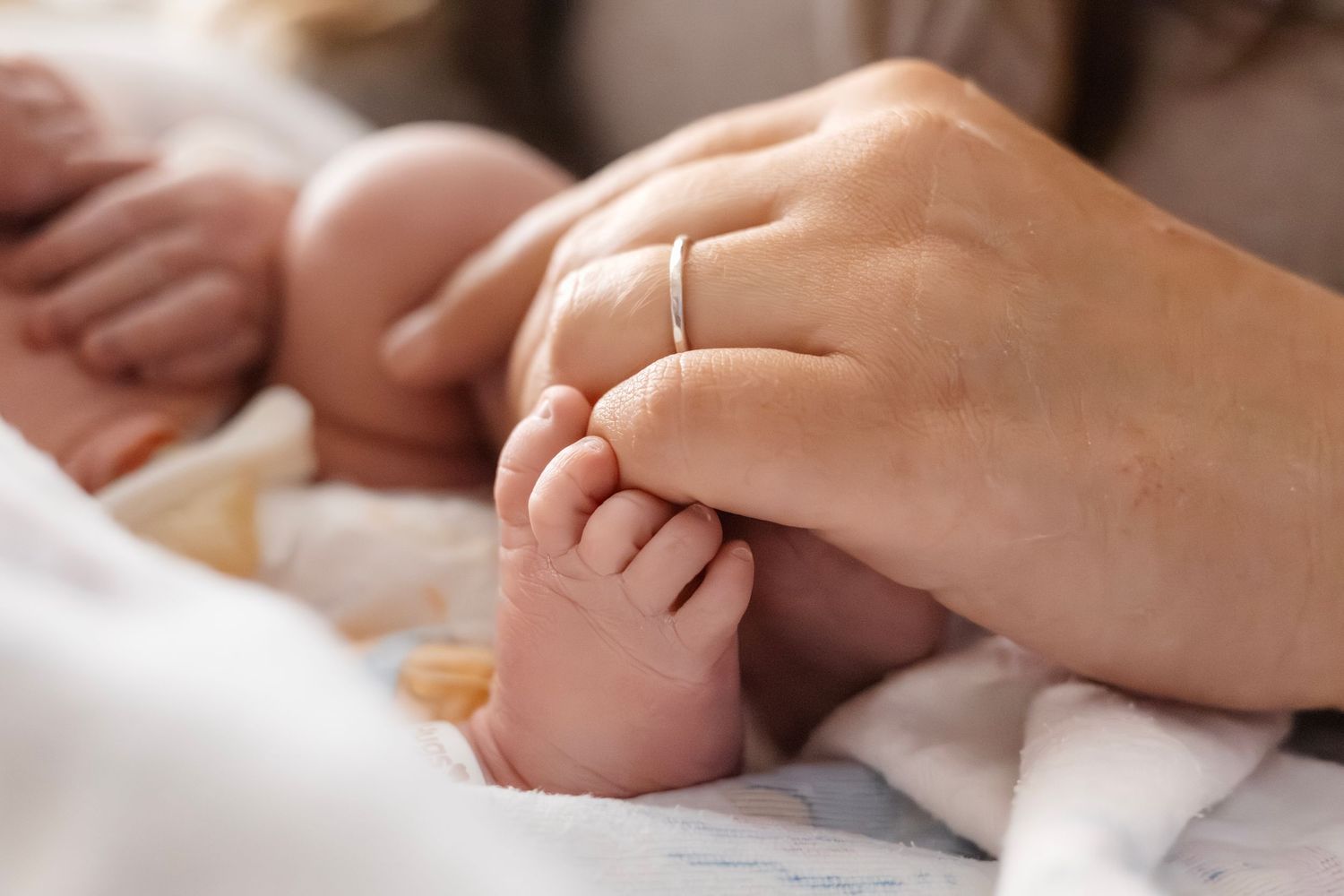 Gentle hands caressing newborn baby's tiny feet on white blanket.