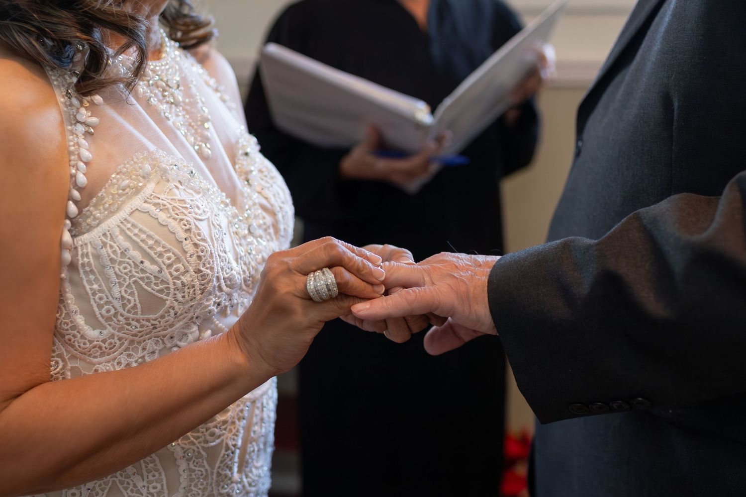 Close-up of hands exchanging wedding rings during ceremony with white lace dress detail visible.