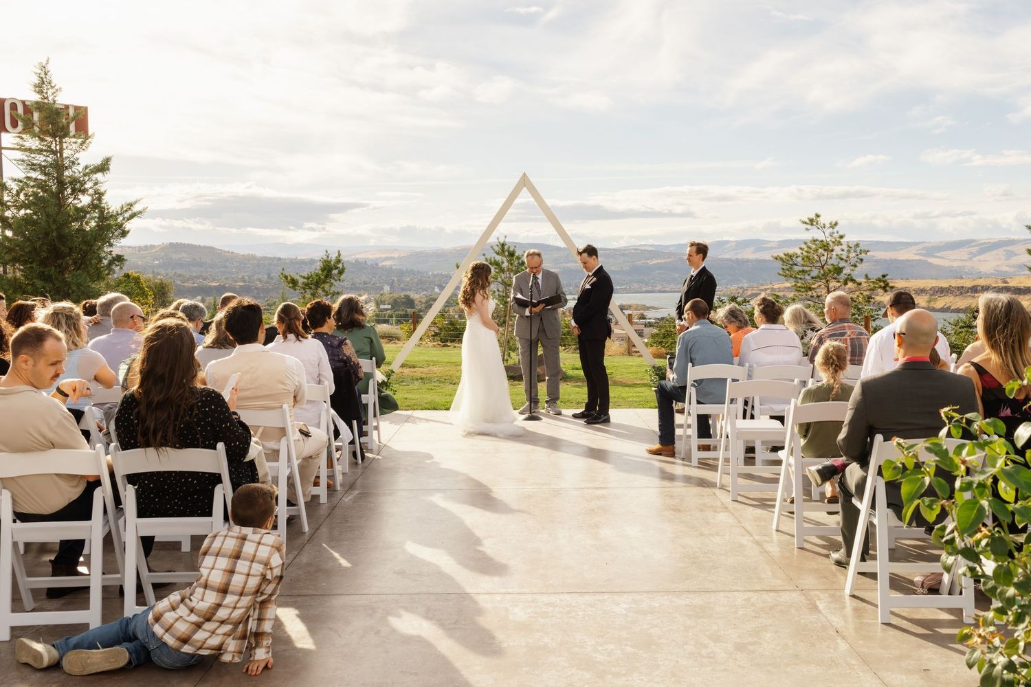 Panoramic view of an outdoor wedding ceremony with white chairs set up overlooking a scenic mountain landscape.