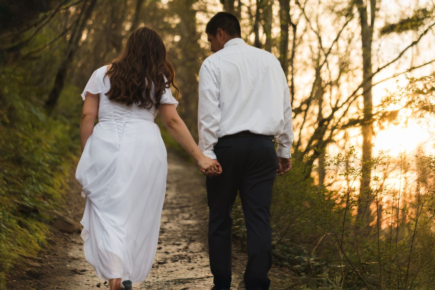 Bride and groom walking hand in hand on a forest path at golden sunset.