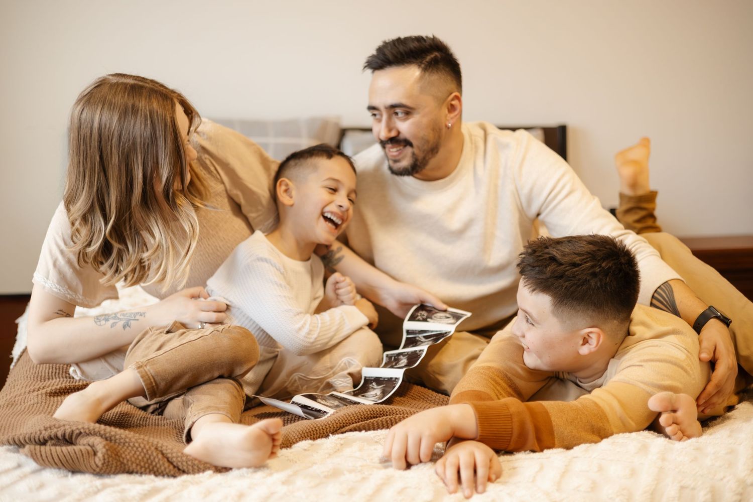 Couple sharing tender moments while looking at ultrasound photos together on a bed.