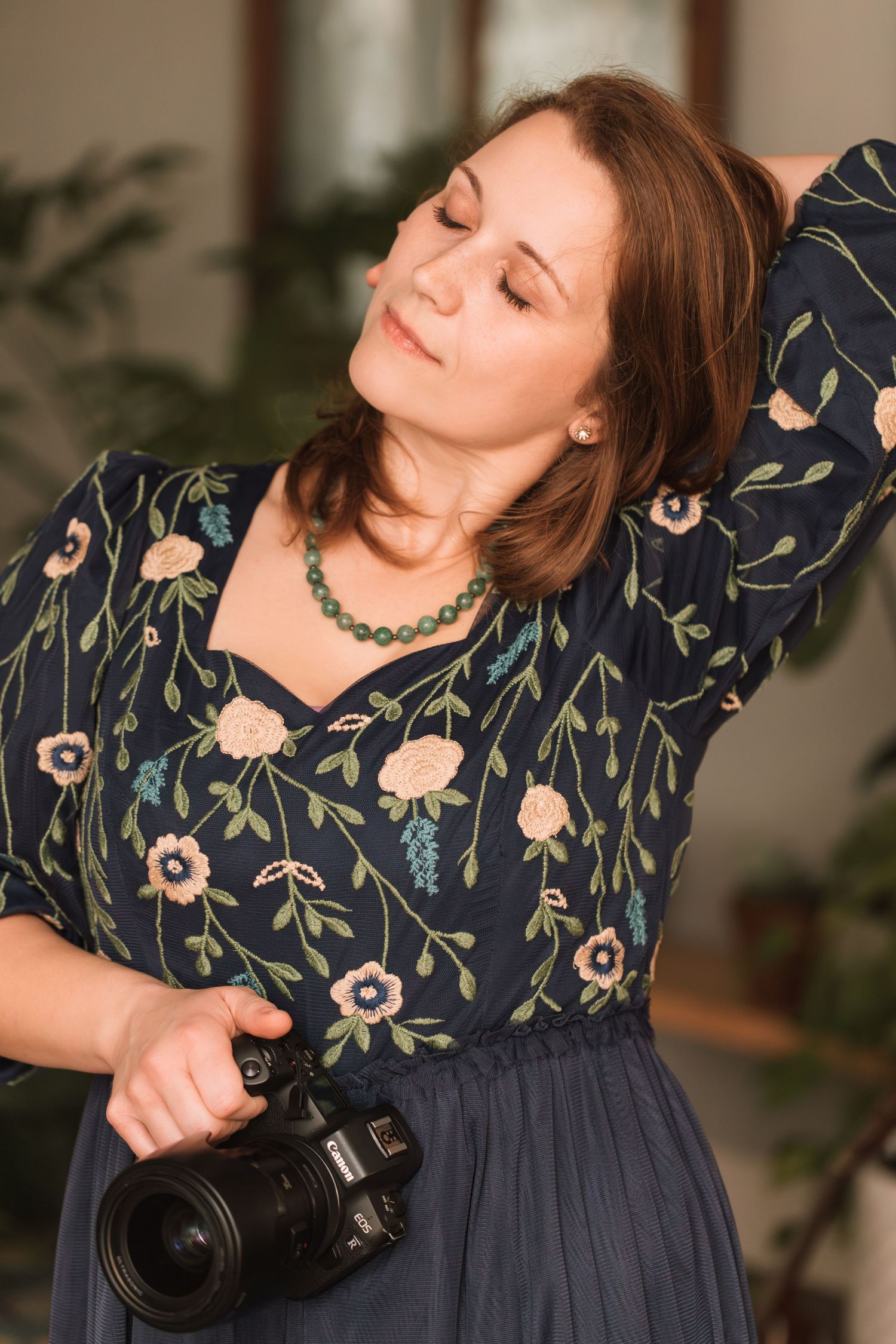 Person wearing navy floral dress poses gracefully with camera in indoor setting.