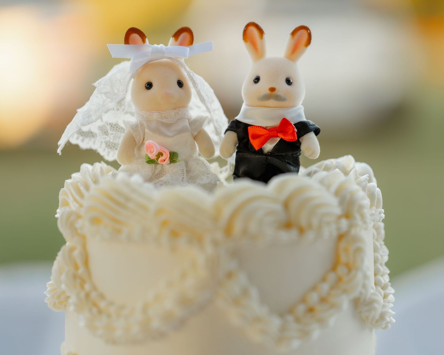 White ceramic wedding cake toppers featuring adorable cat figurines decorated with formal attire on a lace base.