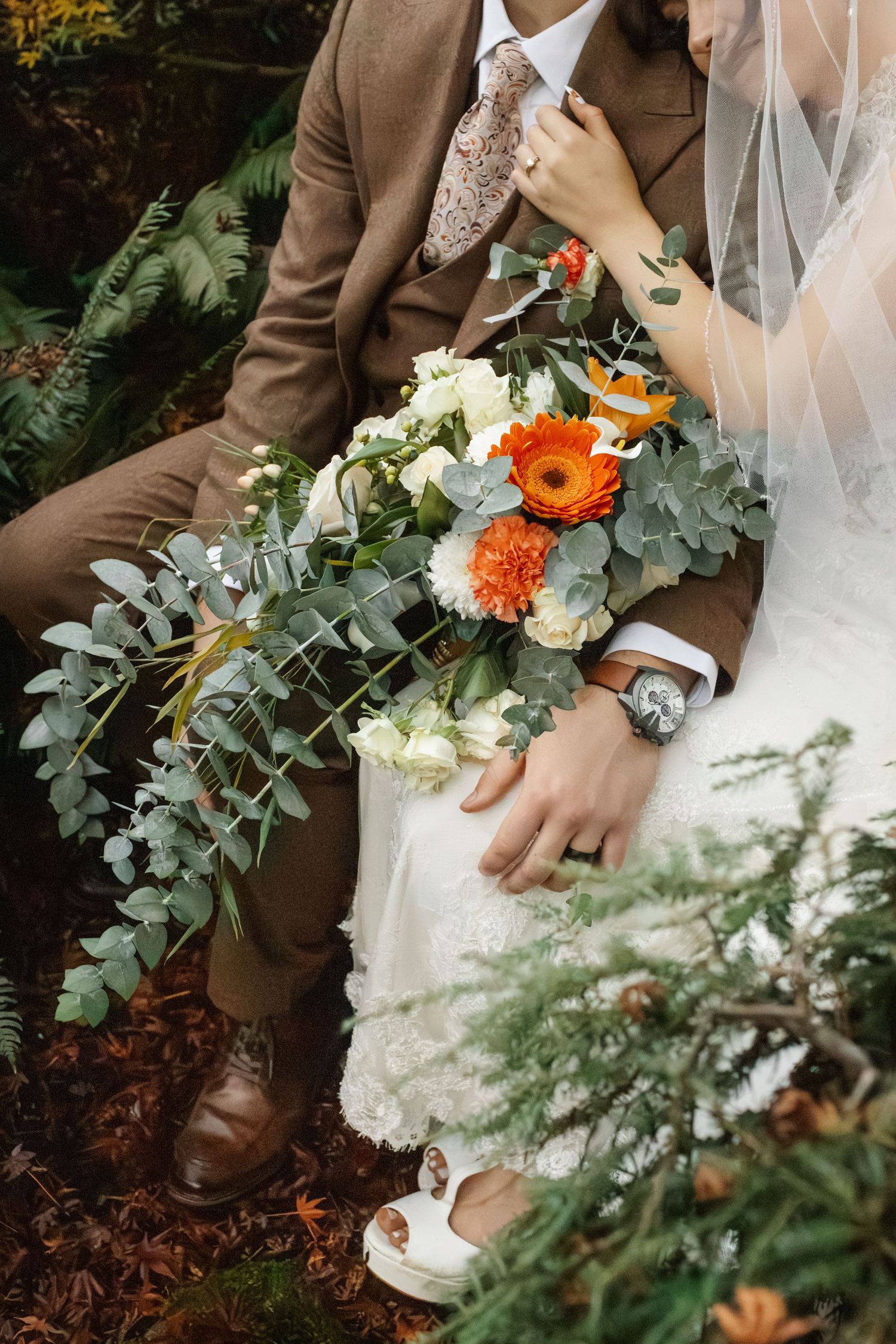 Close-up of wedding bouquet with orange flowers and eucalyptus leaves against brown suit.