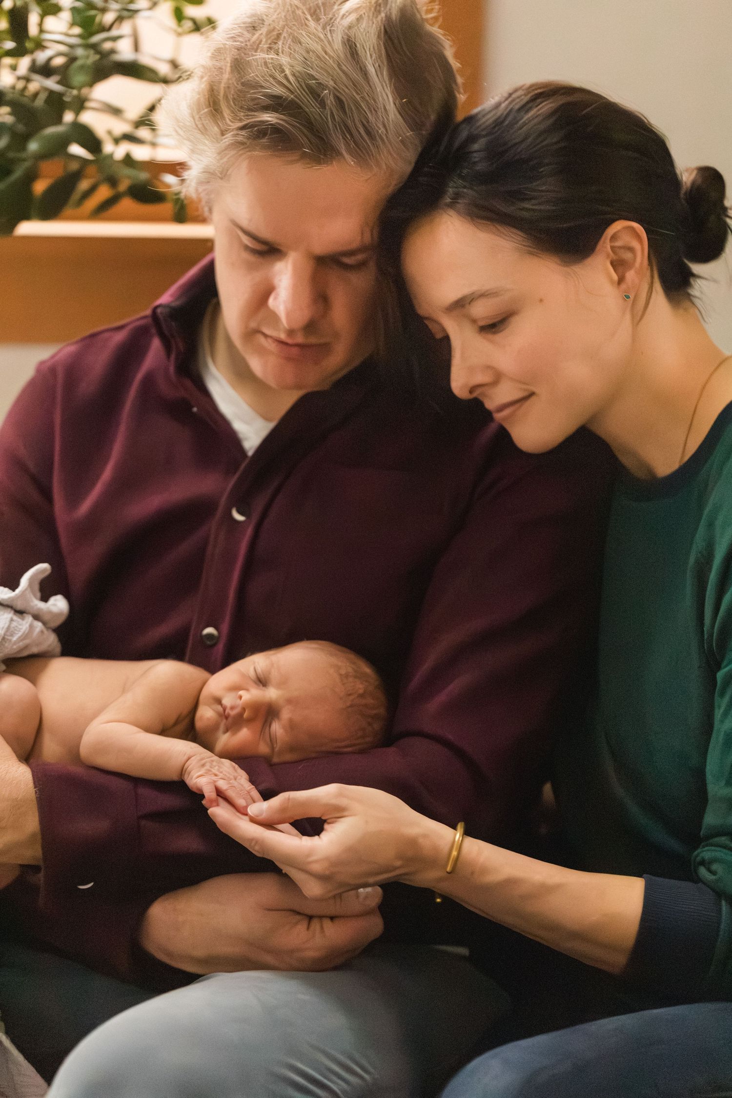 Two parents lovingly cradle their sleeping newborn baby together in a warm, cozy home setting.