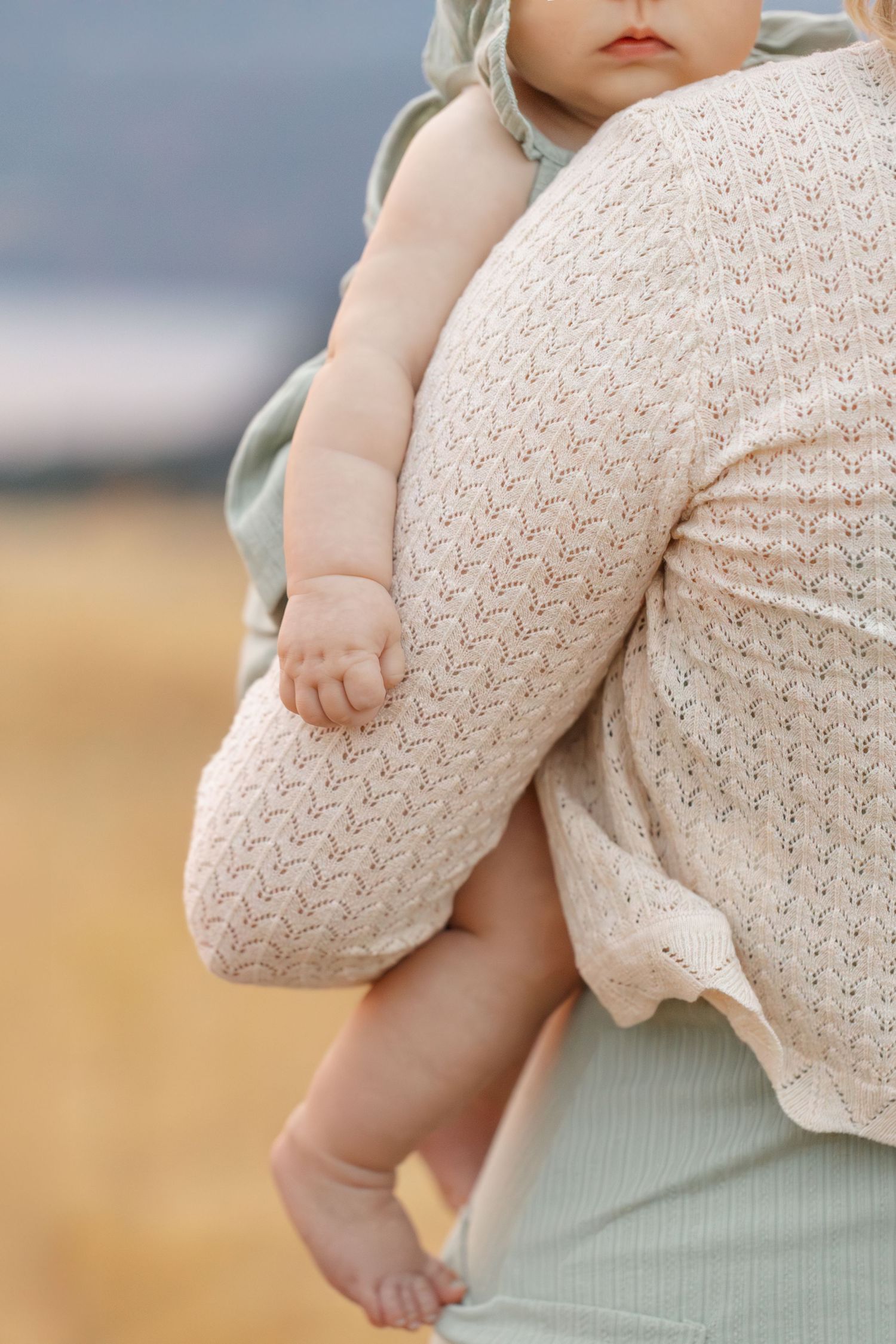 Baby wearing knit sweater being held against soft mint green fabric.