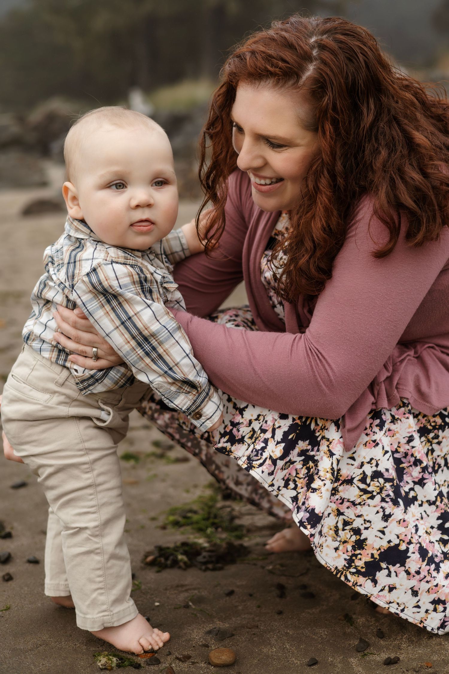 Sweet candid moment shared between parent and baby on a rocky beach.