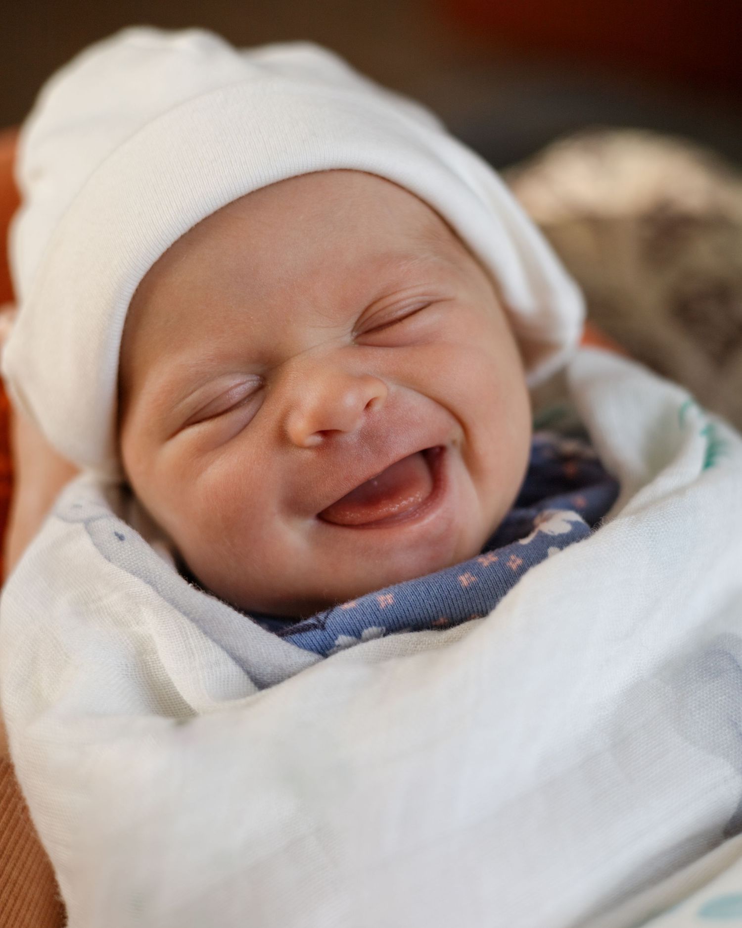 Newborn in white cap showing joyful expression while sleeping.