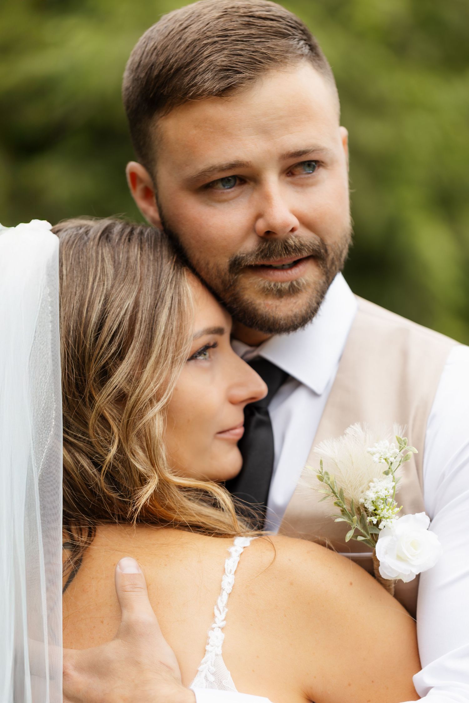 A romantic wedding couple shares an intimate moment outdoors with natural greenery in the background.