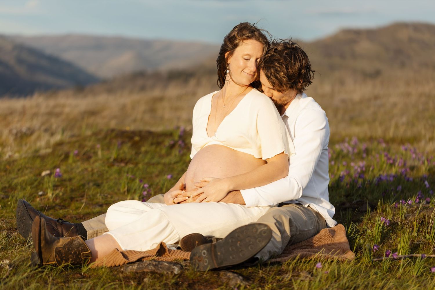 Couple lounges together on grass overlooking a scenic mountain landscape.