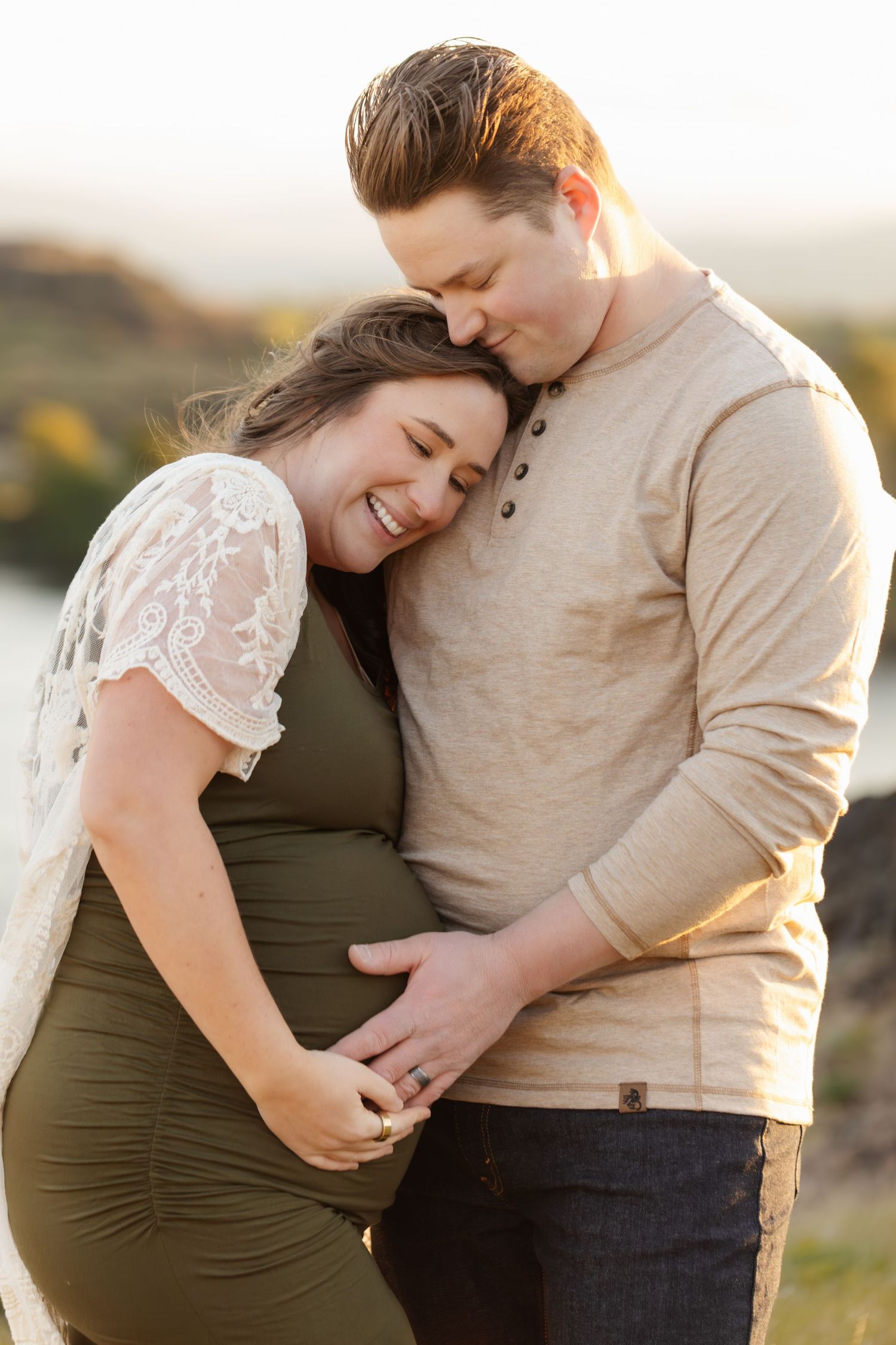 Intimate moment between couple during outdoor maternity photo session at golden hour.