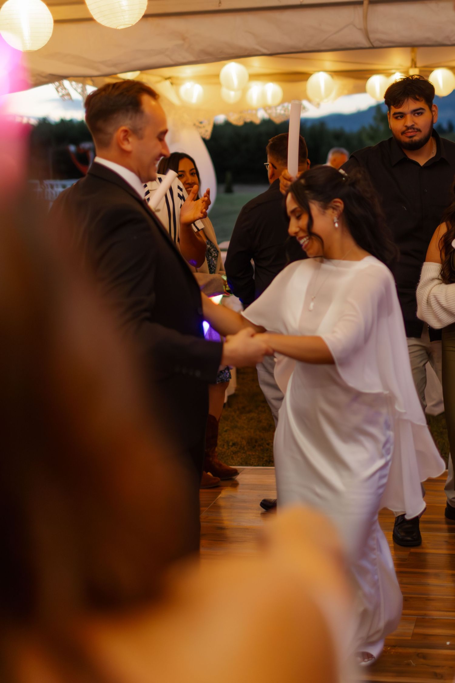 A couple dances together at an evening wedding reception under glowing paper lanterns.