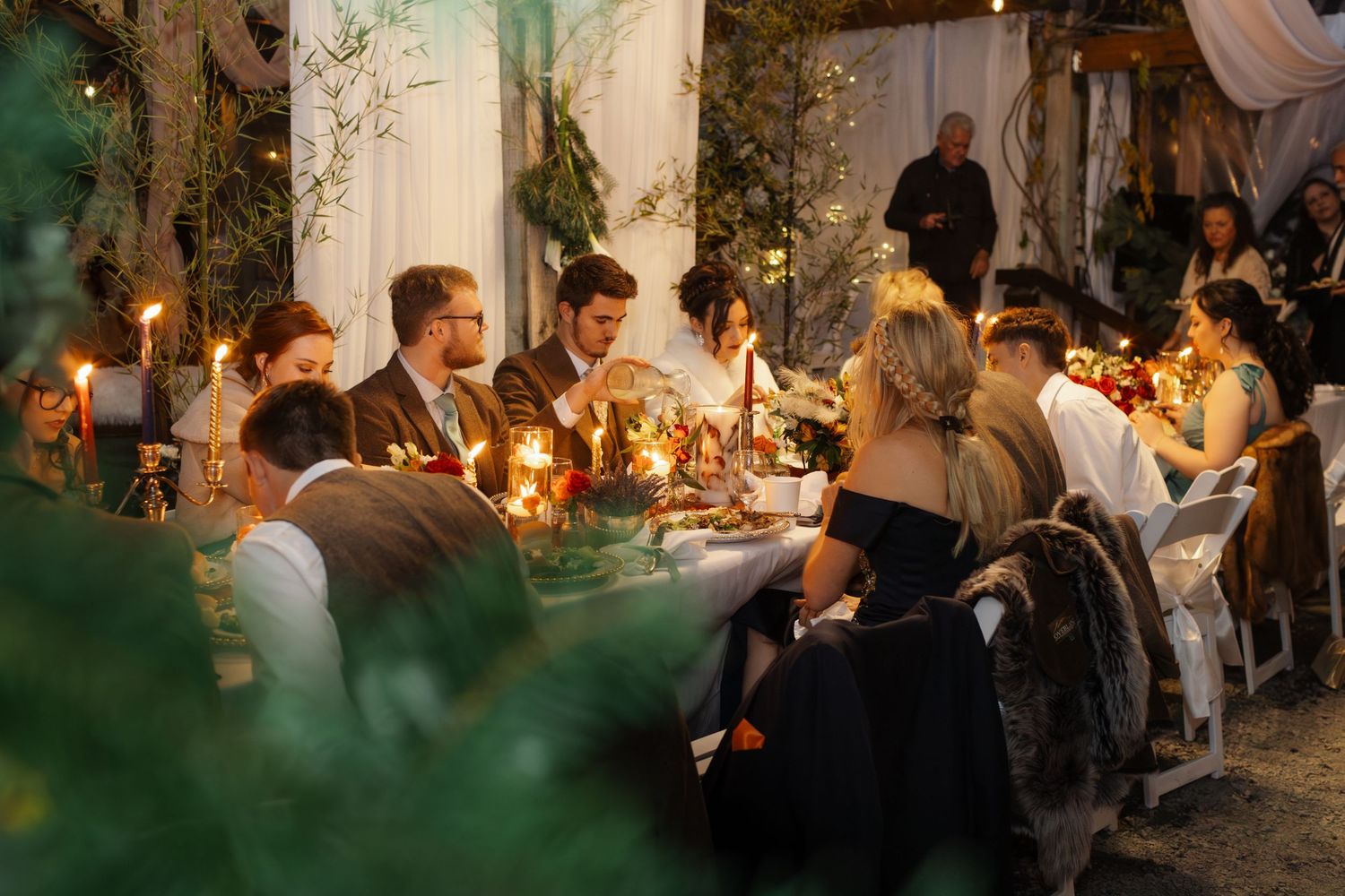 Guests enjoy an intimate candlelit dinner party in a romantic garden setting with glowing ambiance and greenery.
