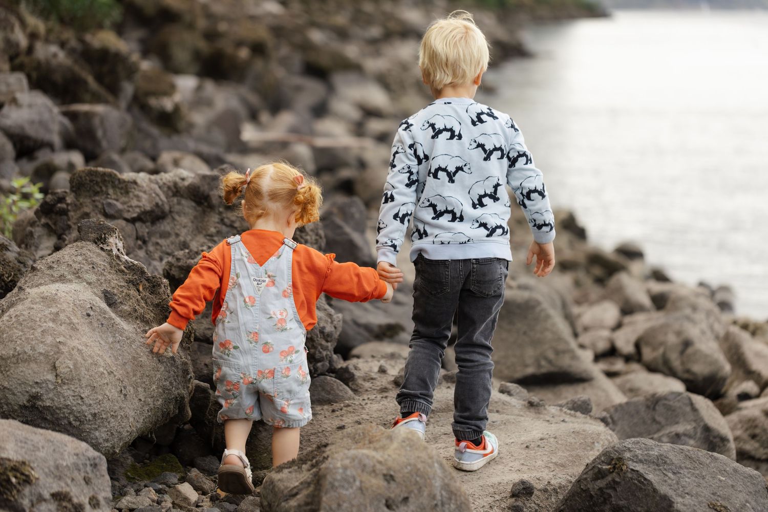 Two children exploring rocky shoreline wearing matching orange and patterned outfits.