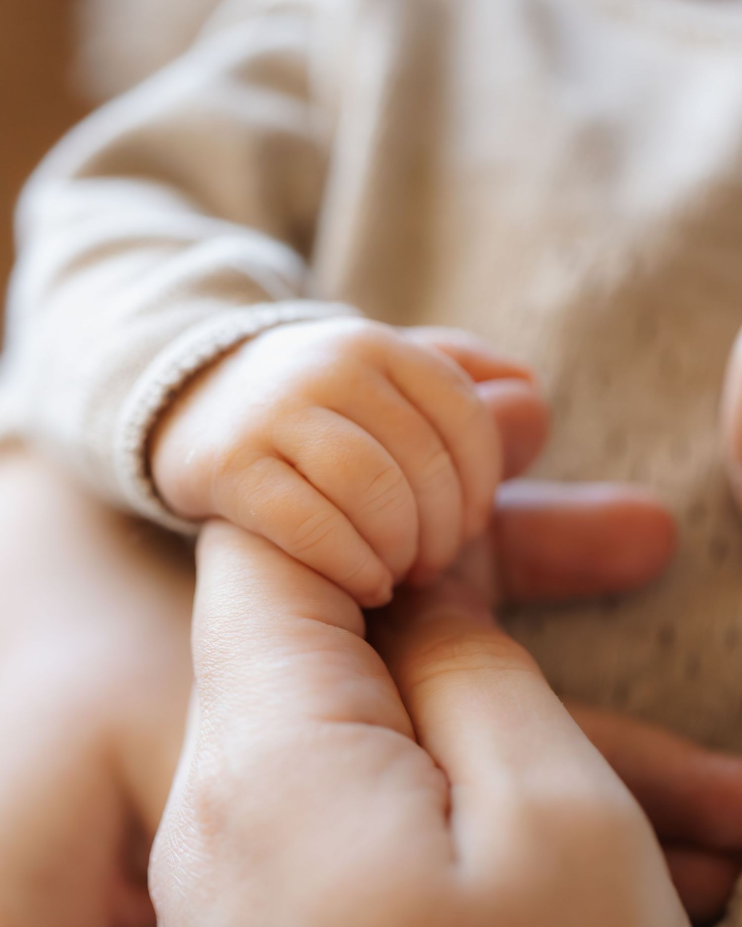 Close-up of tiny newborn baby fingers grasping gently.