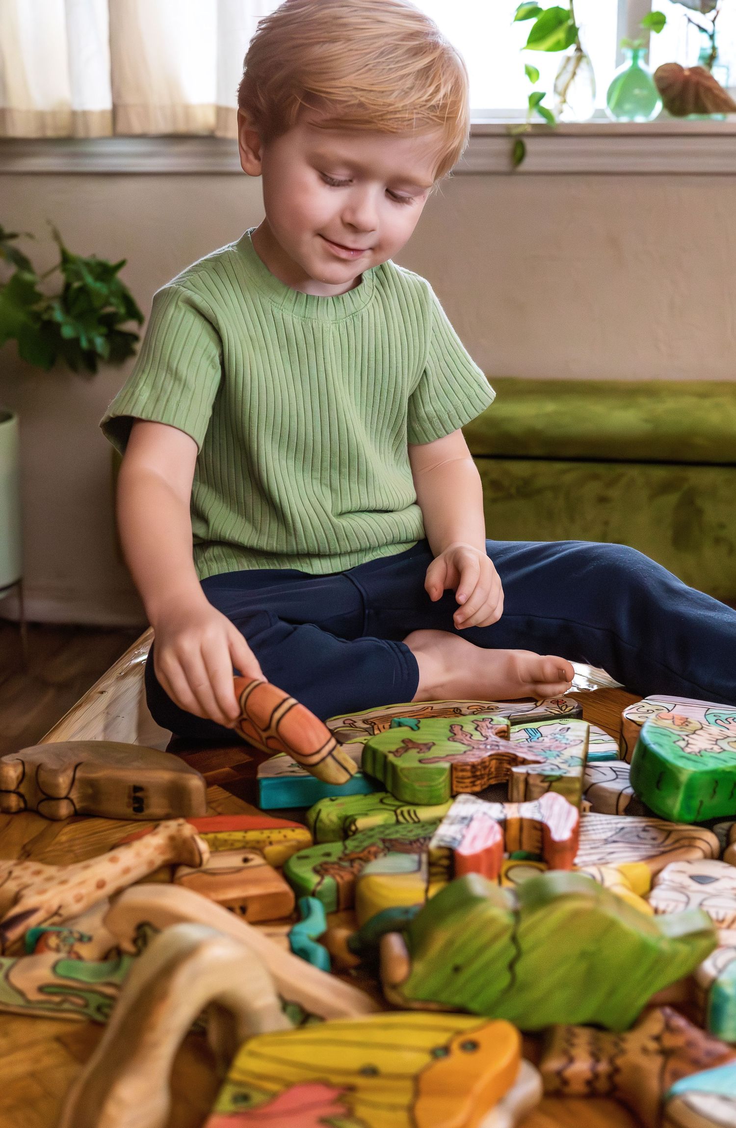 Young child in green shirt playing with wooden toys and craft supplies at a table.