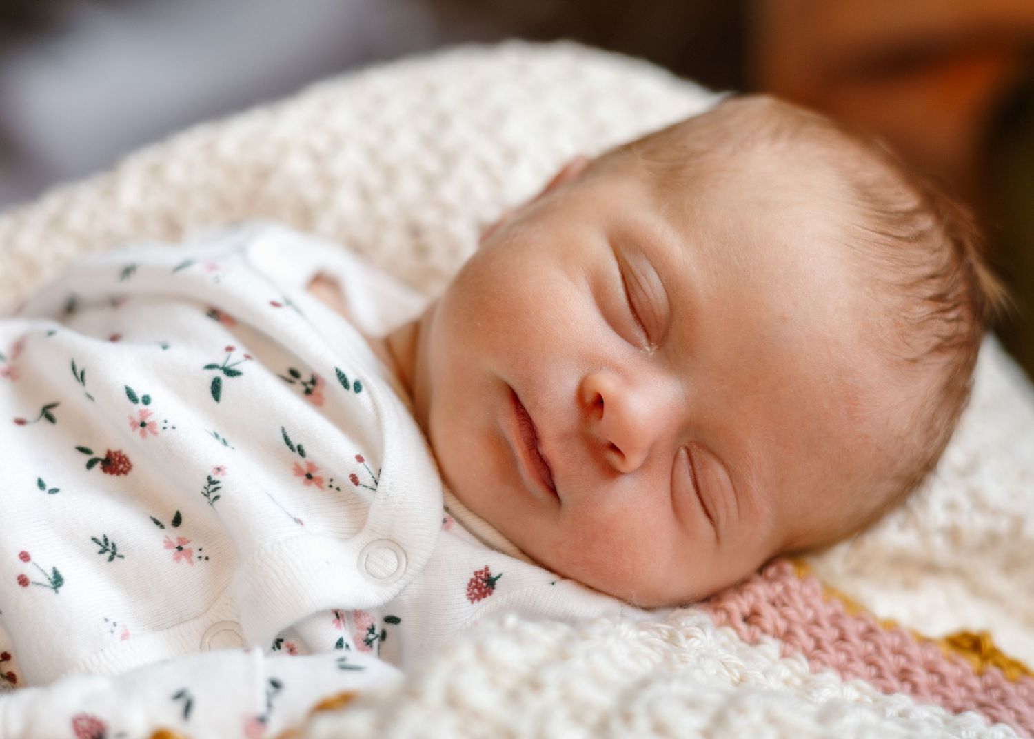 Sleeping newborn on textured white blanket wearing floral print outfit.