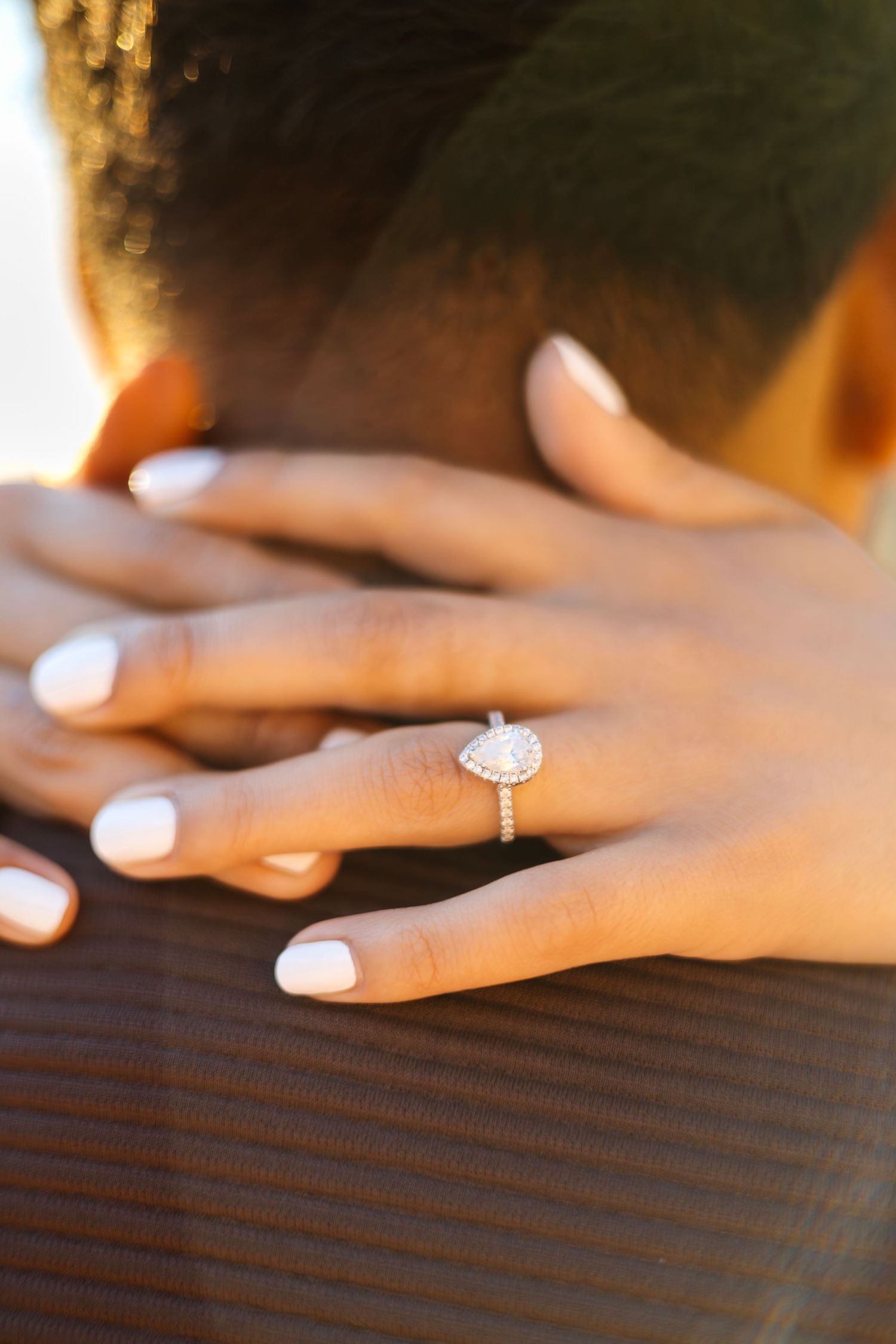 Close-up of a sparkling engagement ring on a hand with white nail polish.