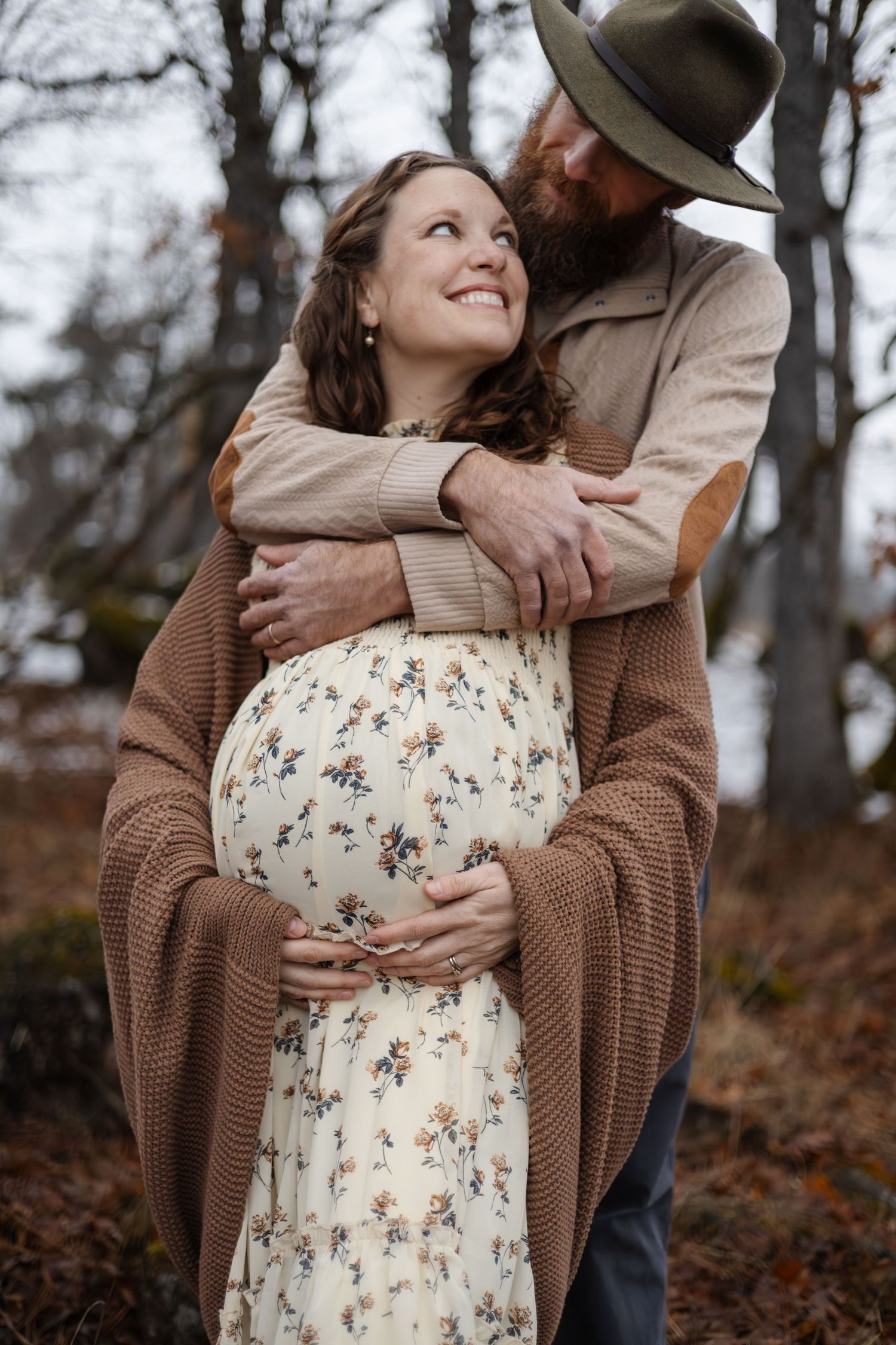 Intimate maternity photo of couple embracing outdoors wearing brown and floral clothing.