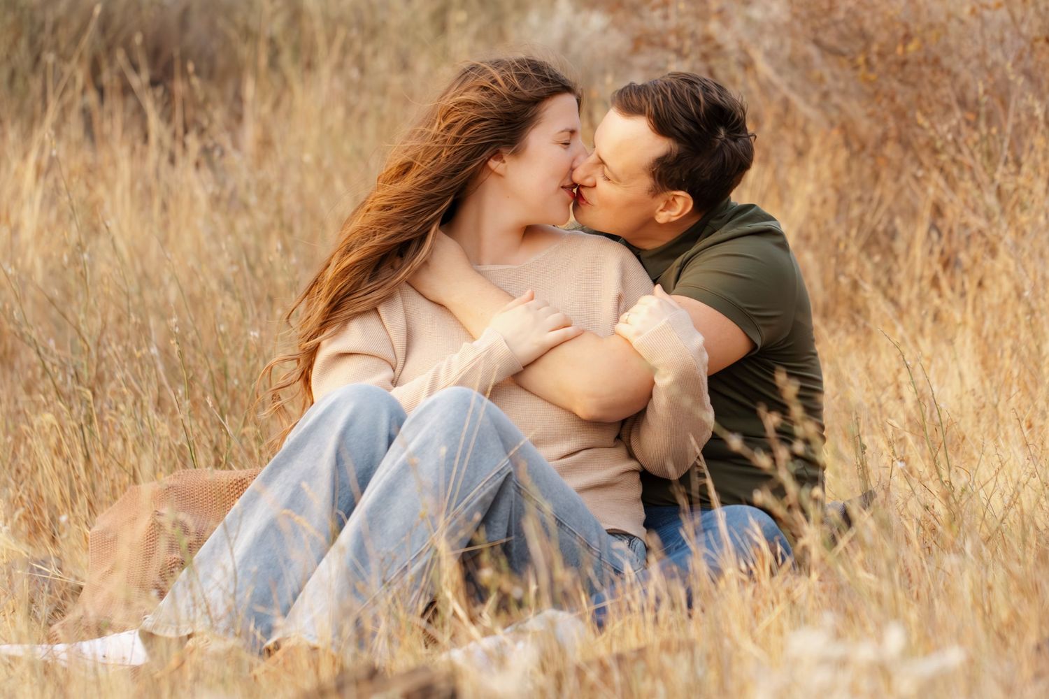 Couple sharing intimate moments in tall dry grass during golden hour.