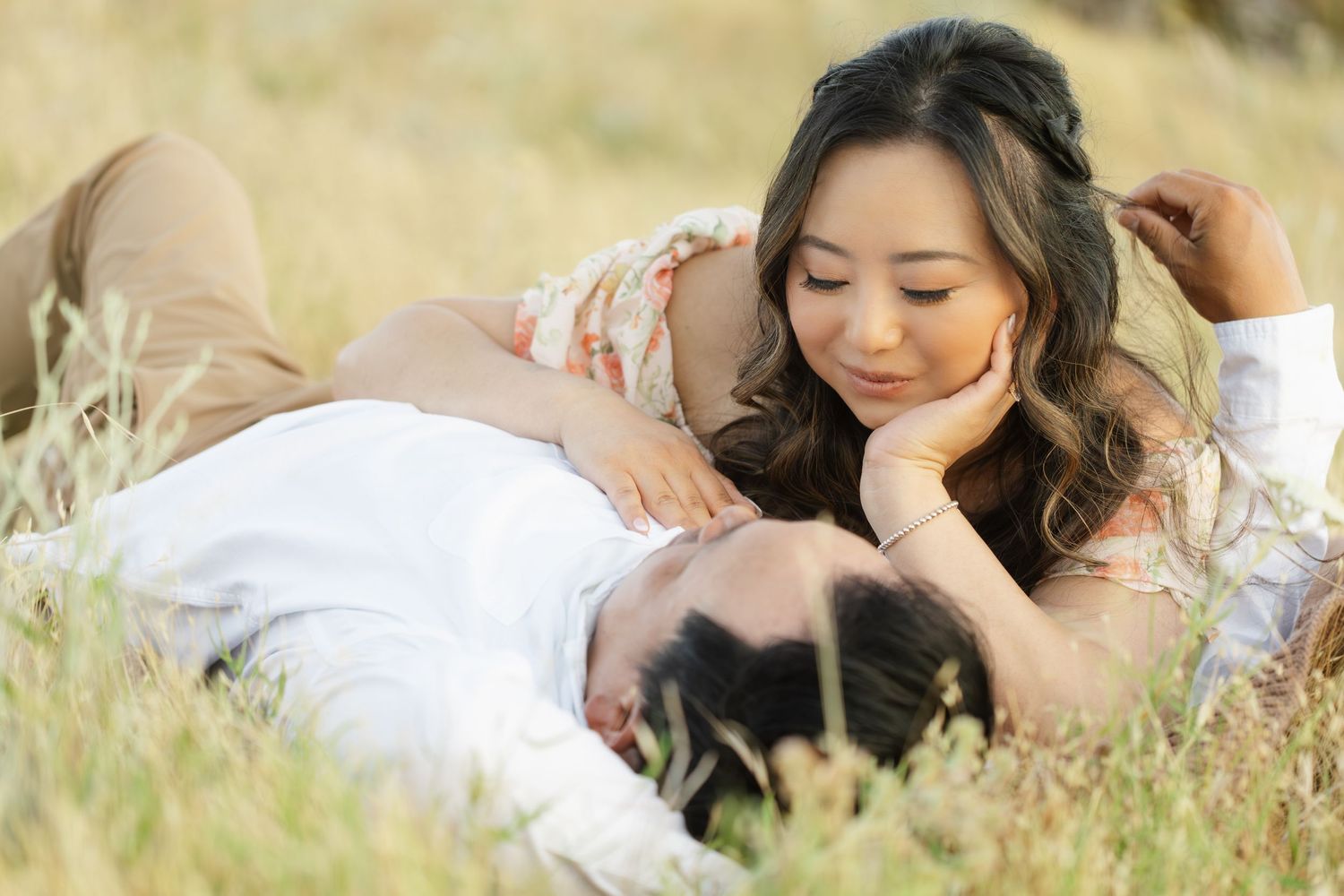 A person in a white dress lying in a meadow of tall grass during golden hour.