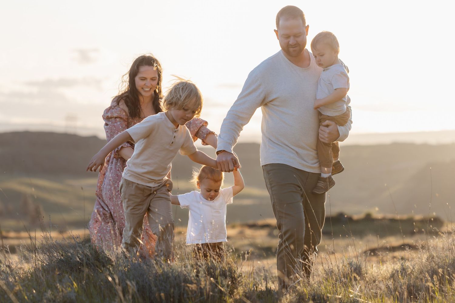 Family running and playing together on a grassy hillside during golden hour.