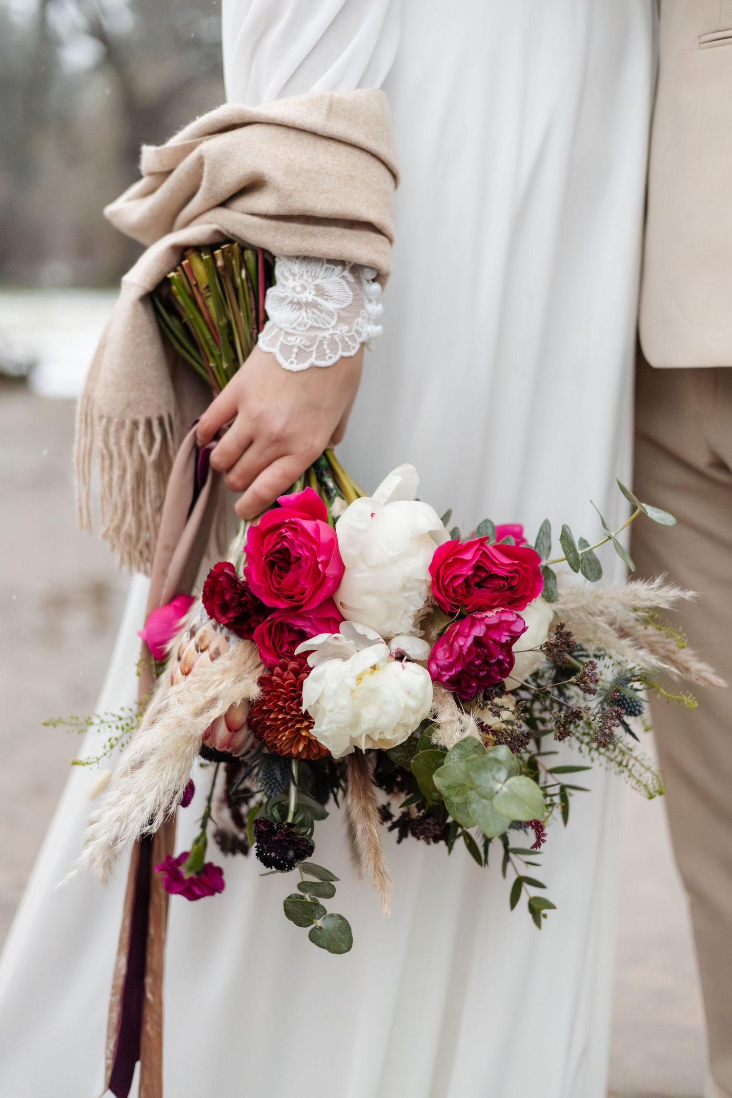 Elegant bridal bouquet with pink and white roses against white dress and beige scarf.