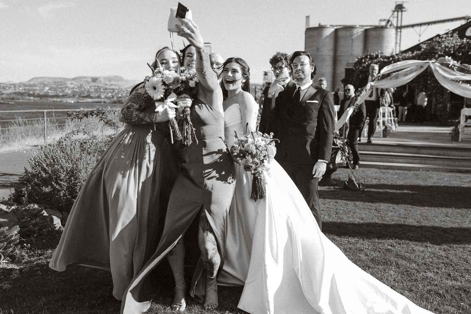 Black and white wedding party group photo taken outdoors with mountains in the background.