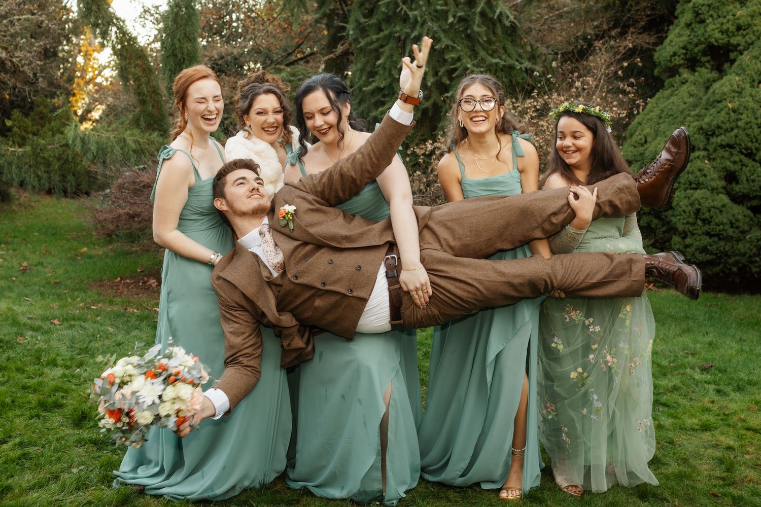 Wedding party in mint green dresses and brown suits posing together outdoors in a garden setting.