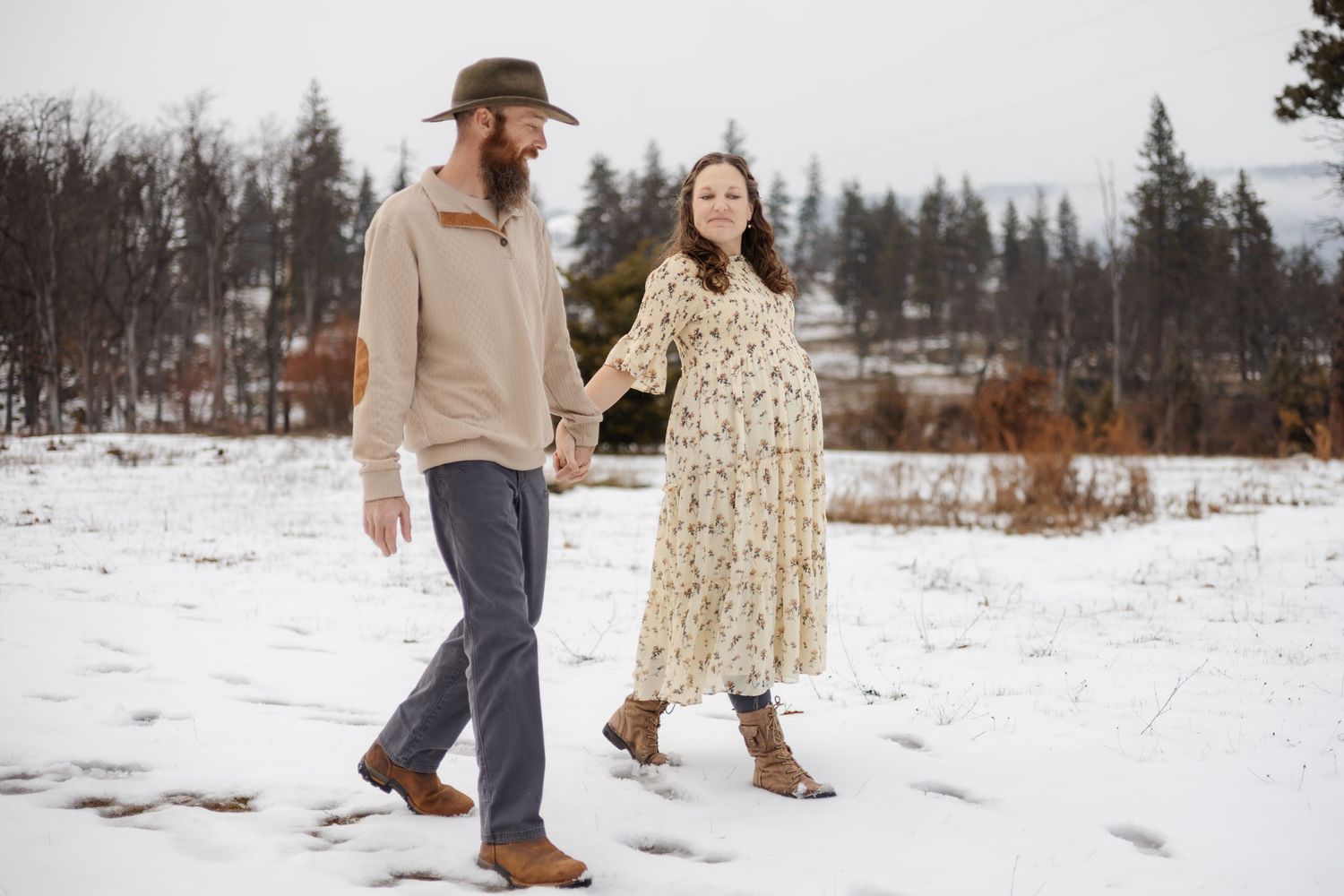 Family walking through snowy winter landscape with evergreen trees in background.