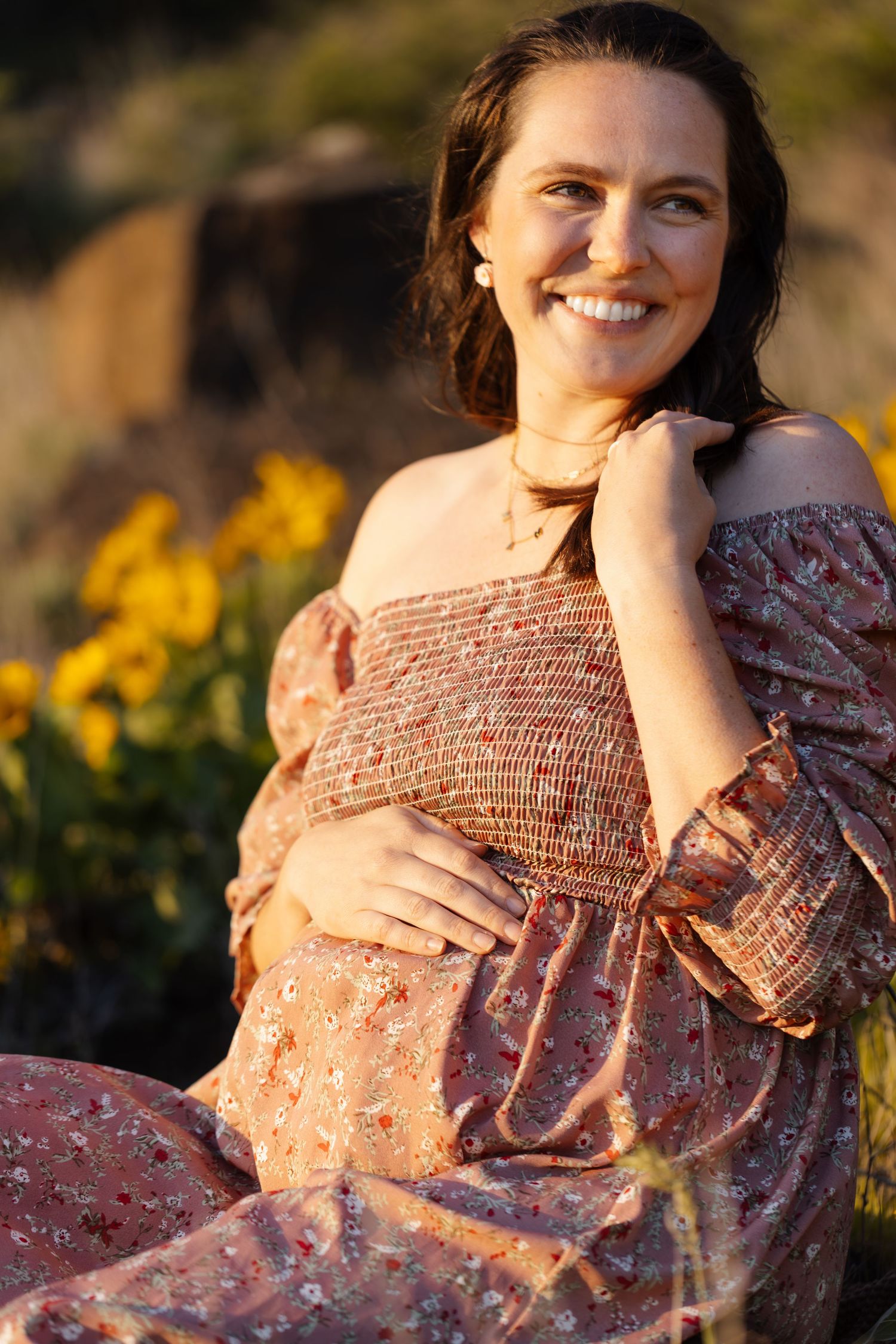 Maternity photoshoot in floral dress among yellow wildflowers at sunset.