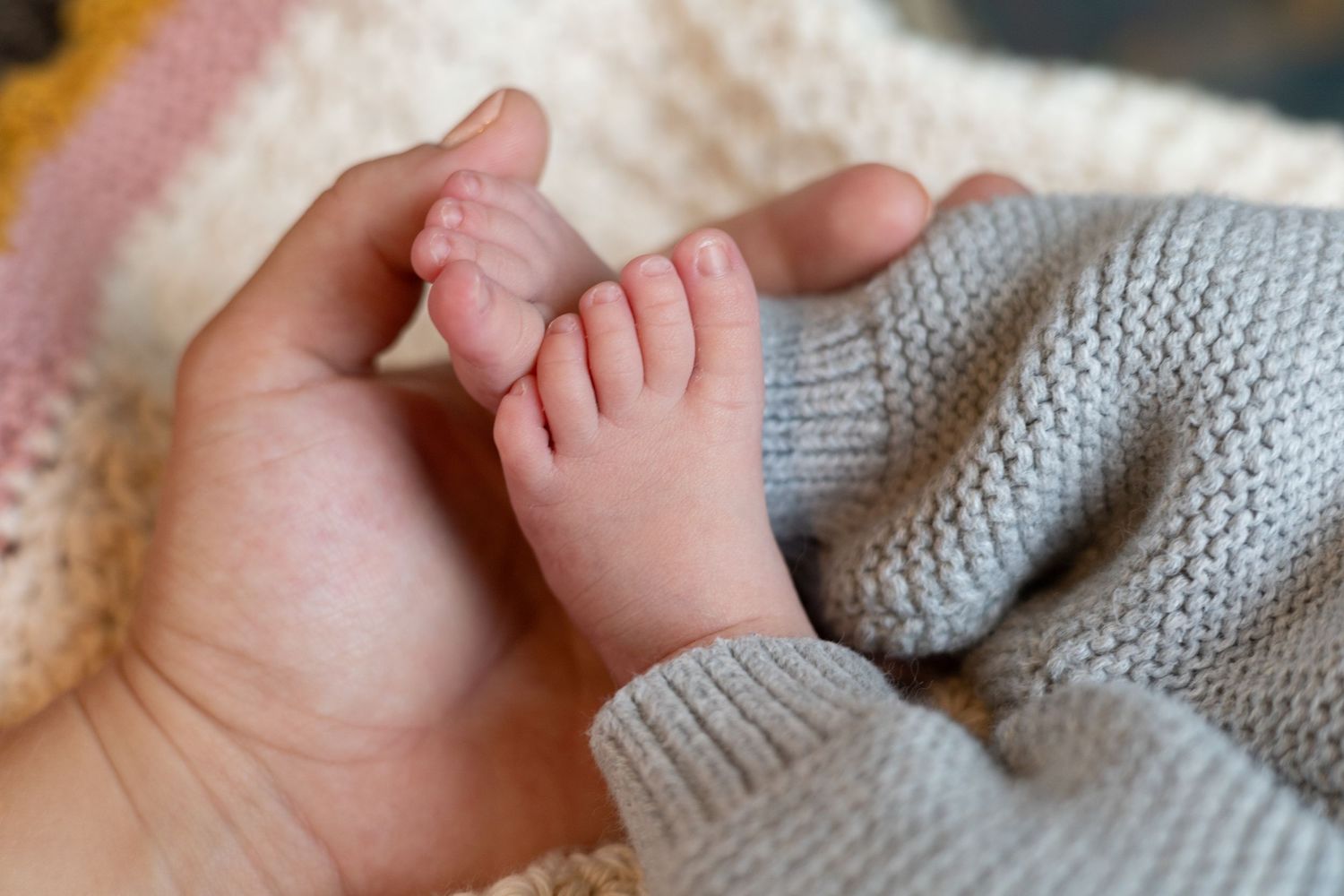 Close-up of baby's tiny hand and feet against gray knit fabric.