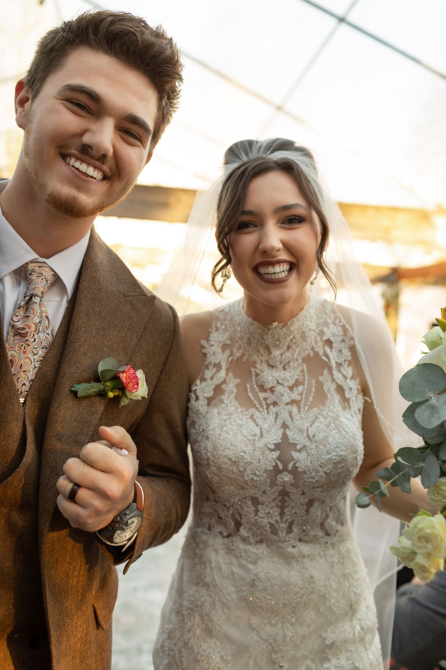 Happy newlyweds share a candid moment in brown tweed suit and lace wedding dress with eucalyptus bouquet.