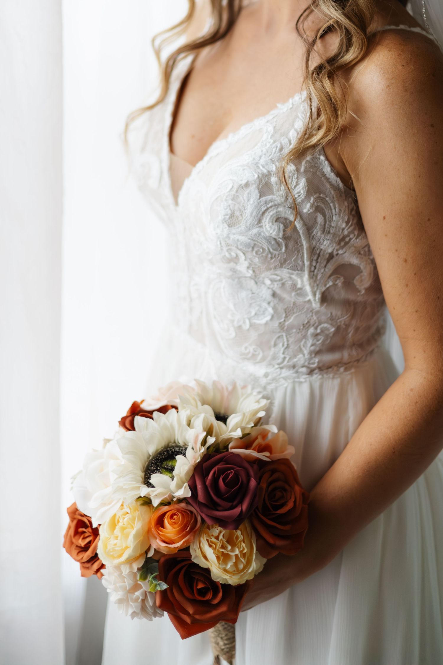 Close-up view of a white lace wedding dress bodice with a burgundy and cream rose bouquet.