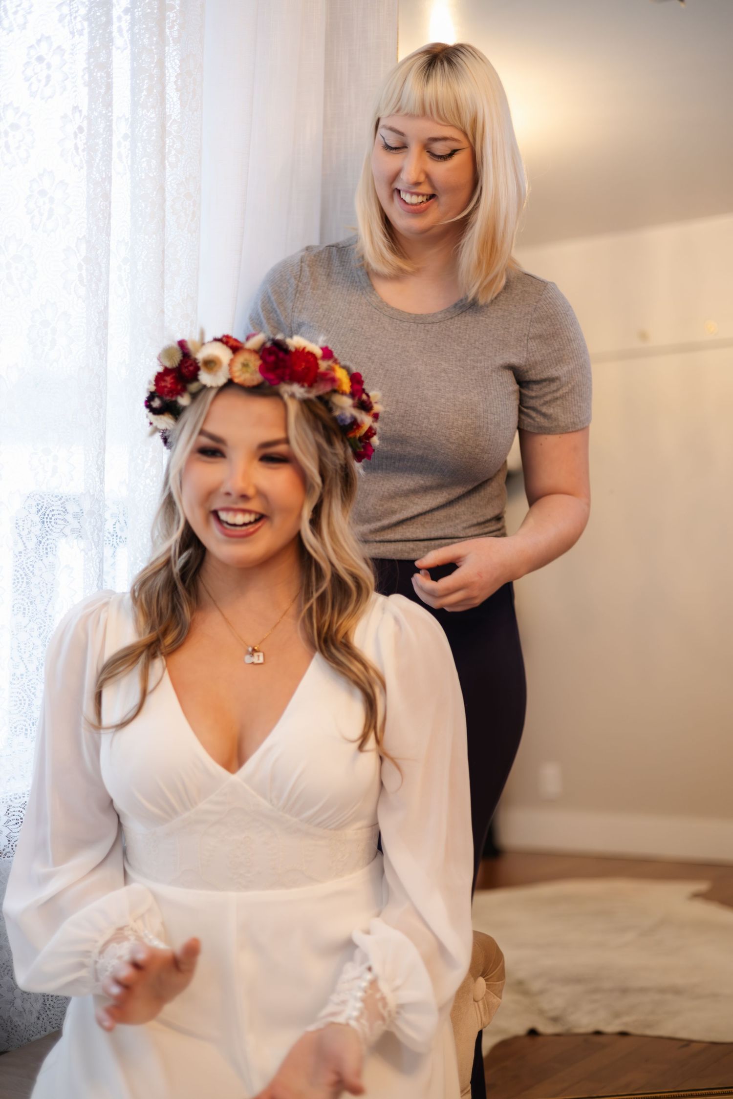 Final wedding preparations as a woman in white gets her hair styled with a floral crown.