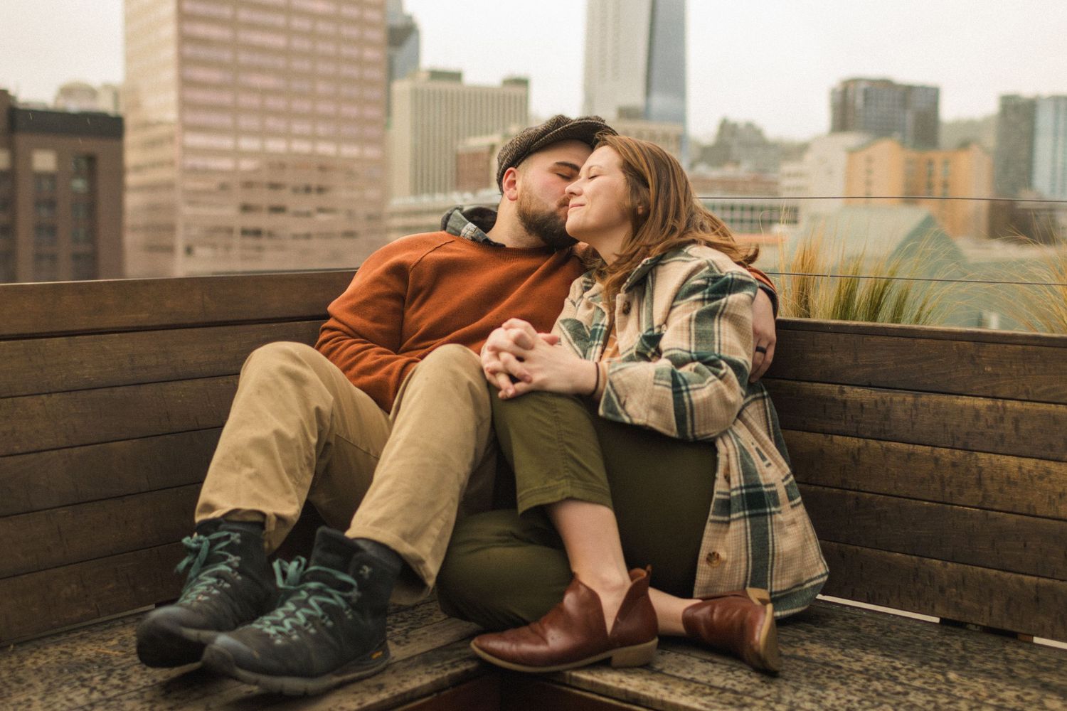 Couple sitting close together on wooden bench against urban cityscape backdrop.
