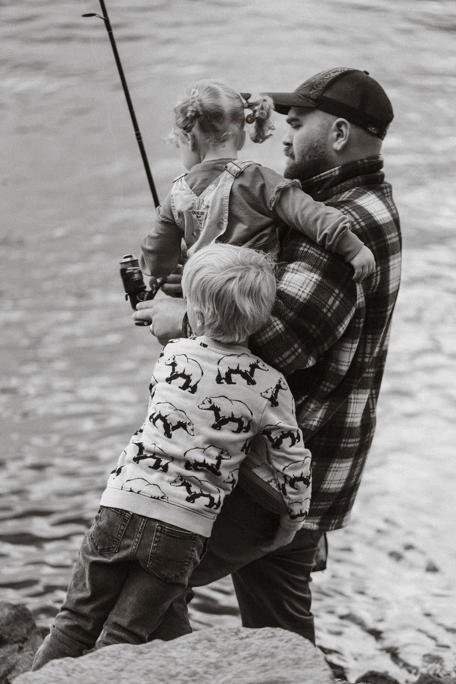 Black and white photo of two people fishing together by the water.