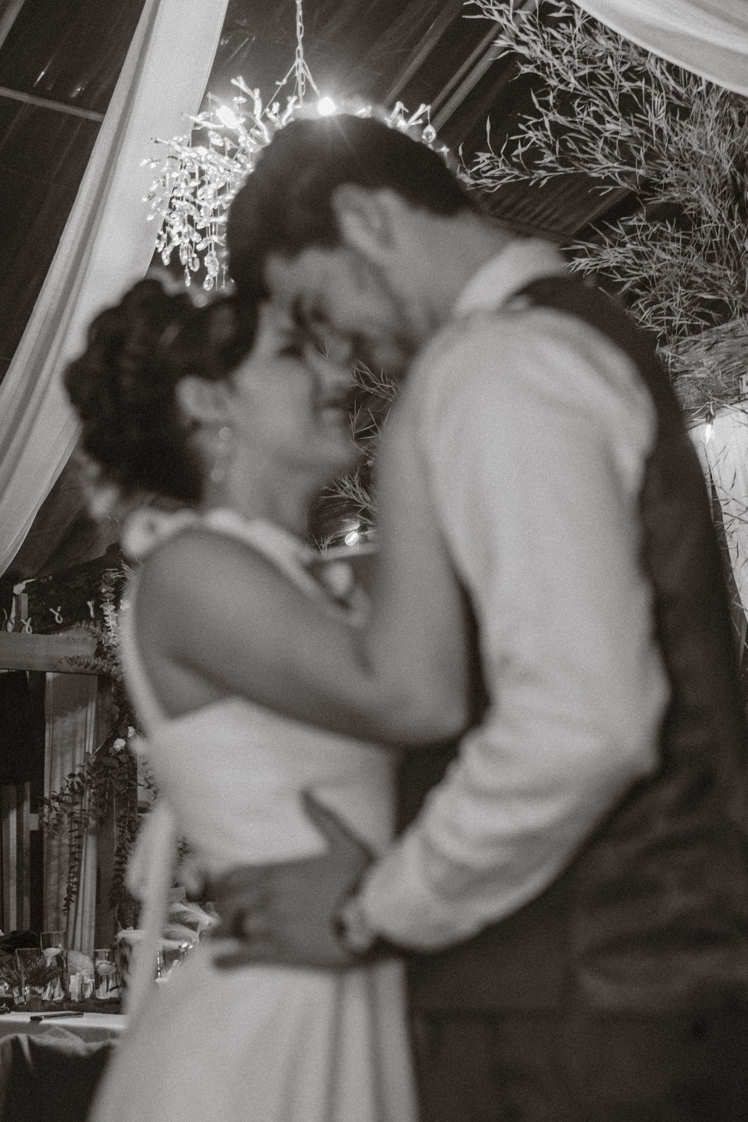 Black and white romantic first dance under twinkling lights and branches.