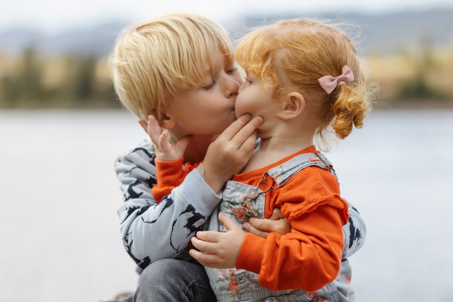 Two young children sharing sweet moment outdoors by the water.