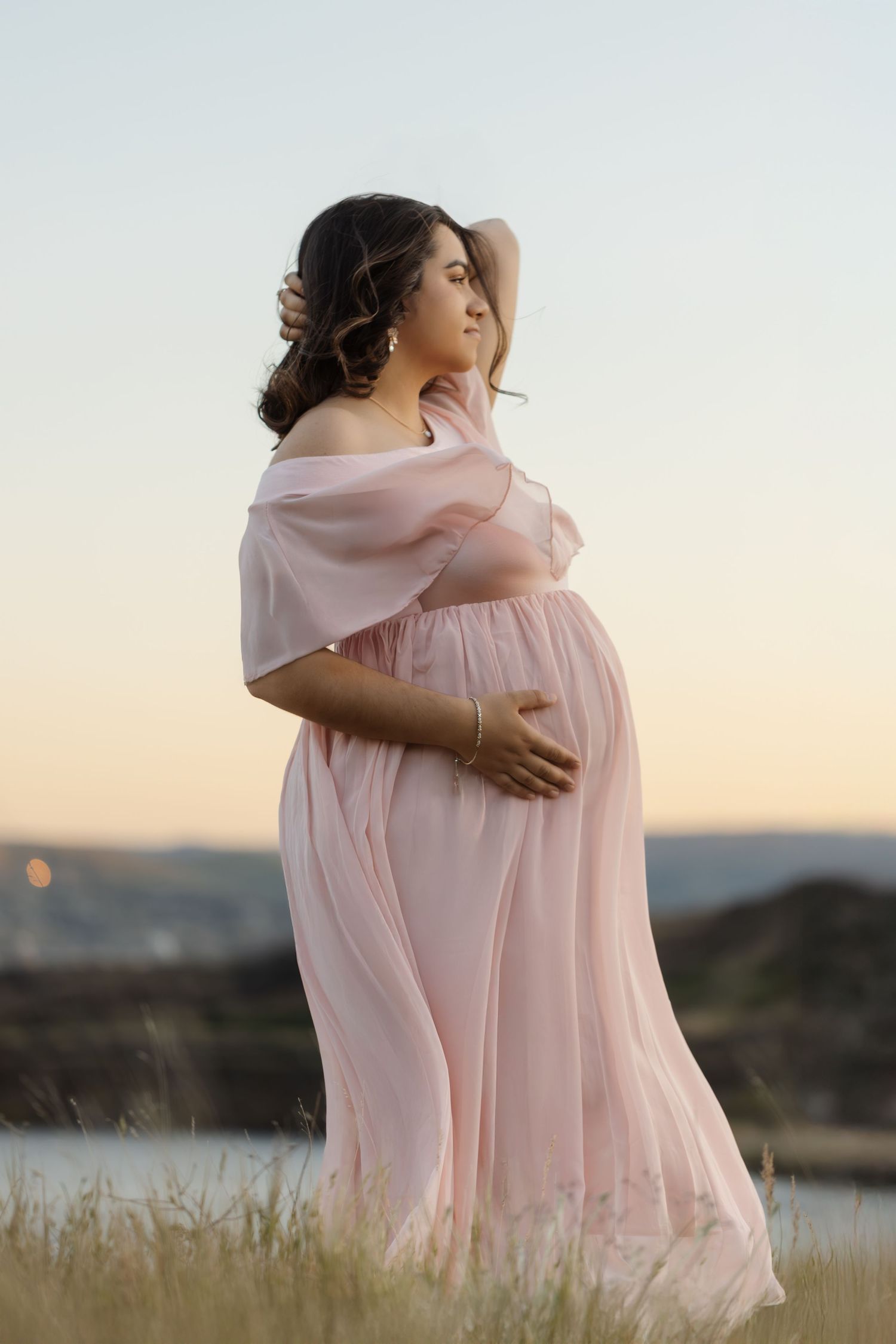 Intimate embrace captured in soft pink dress against golden hour landscape.